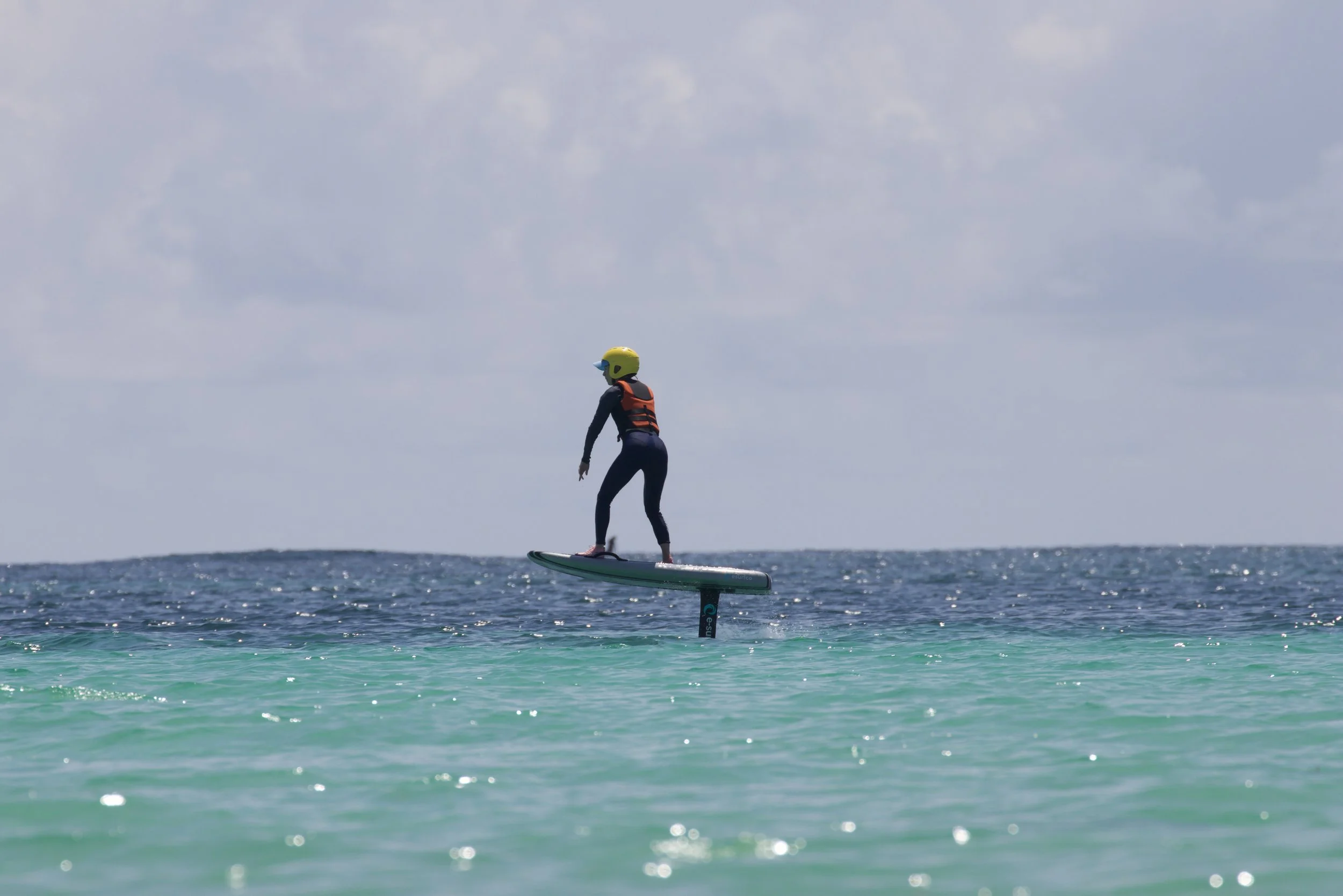 Person in a helmet and life jacket riding a hydrofoil board over the water.