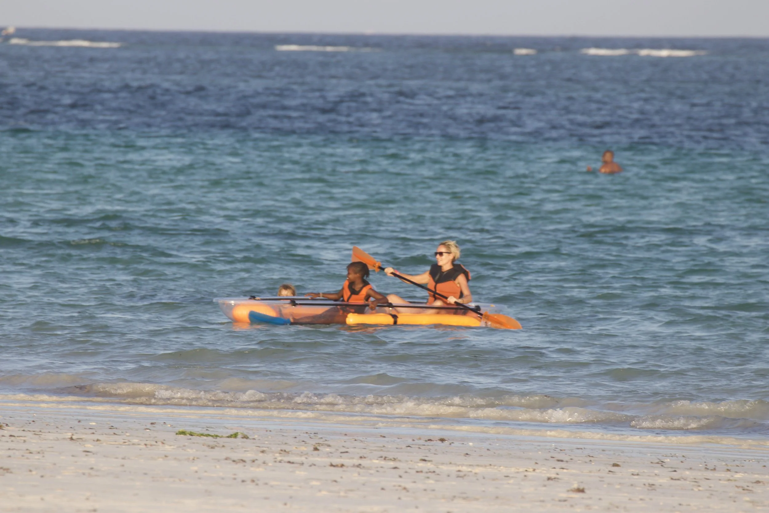 A woman and two young children kayaking in the ocean near a sandy beach.
