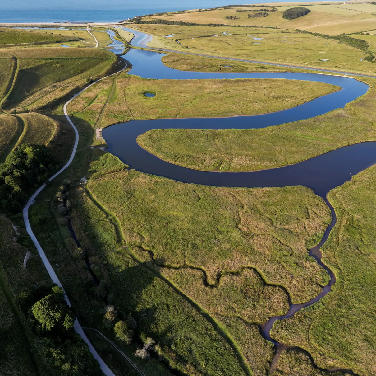 Aerial view of a winding river through green fields and farmland near the coastline.