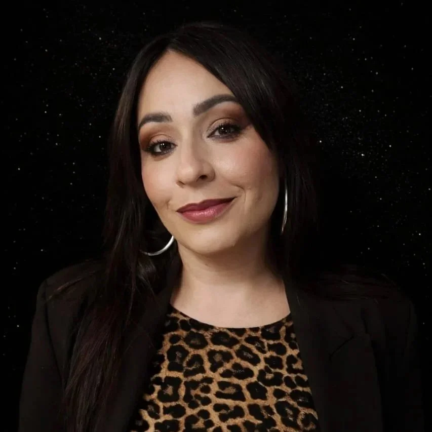 Femme qui sourit brune sur fond noir. Maquillage smocky colorimétrie Almae signature. Tenue haut léopard et veste noir. Créoles argentés.