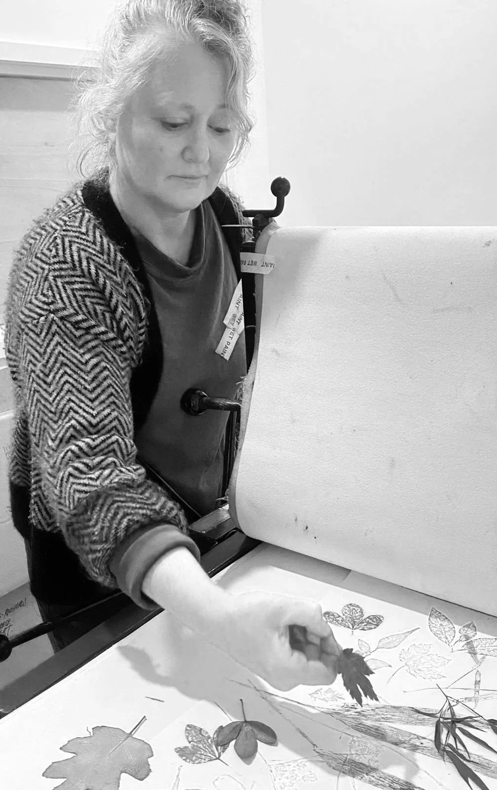 A woman with curly hair looking down at a botanical print with leaves, butterflies, and a flower, on a table in front of her, in black and white.