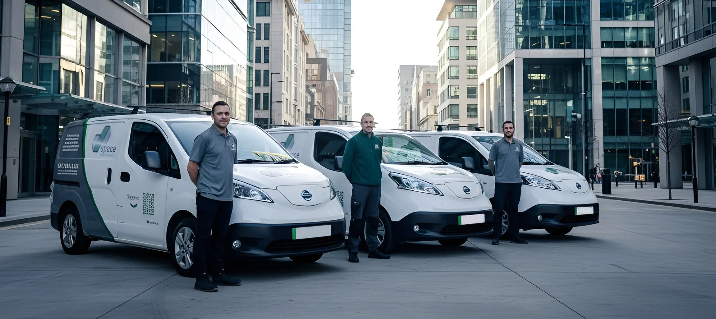 Three delivery workers standing in front of white delivery vans on a city street, with tall modern buildings in the background.