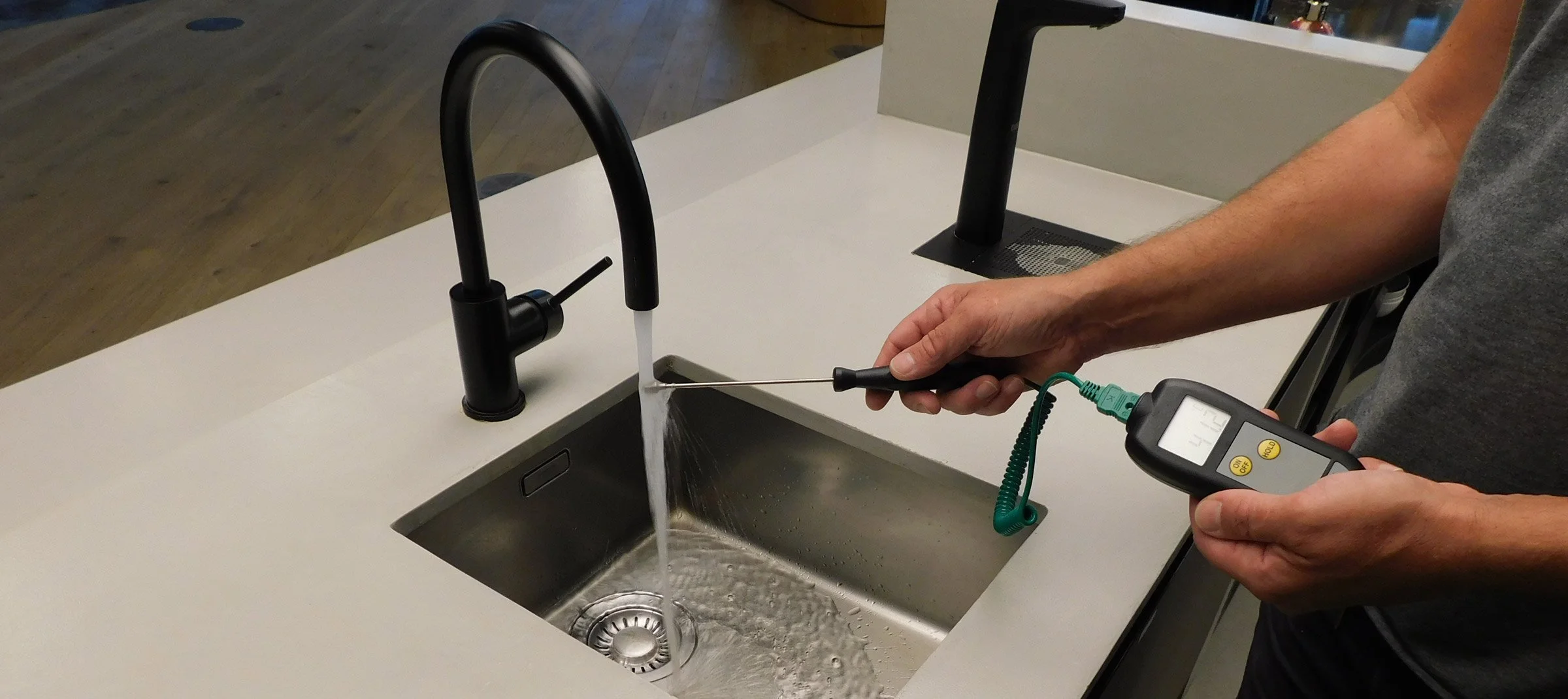 Person inspecting a kitchen sink with a device connected to measure water quality or flow.