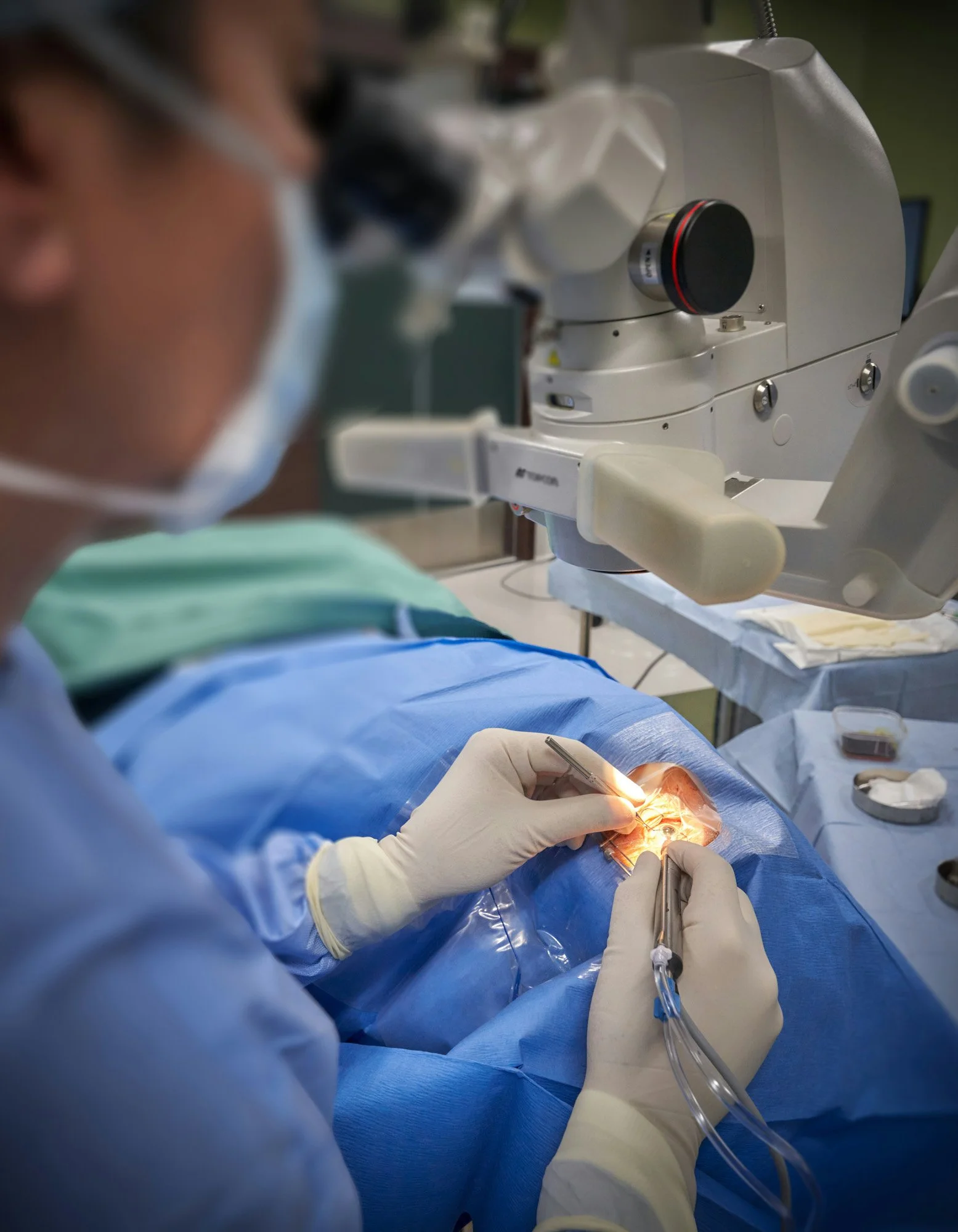 Surgeon in surgical gown and gloves performing a procedure, looking through a microscope.