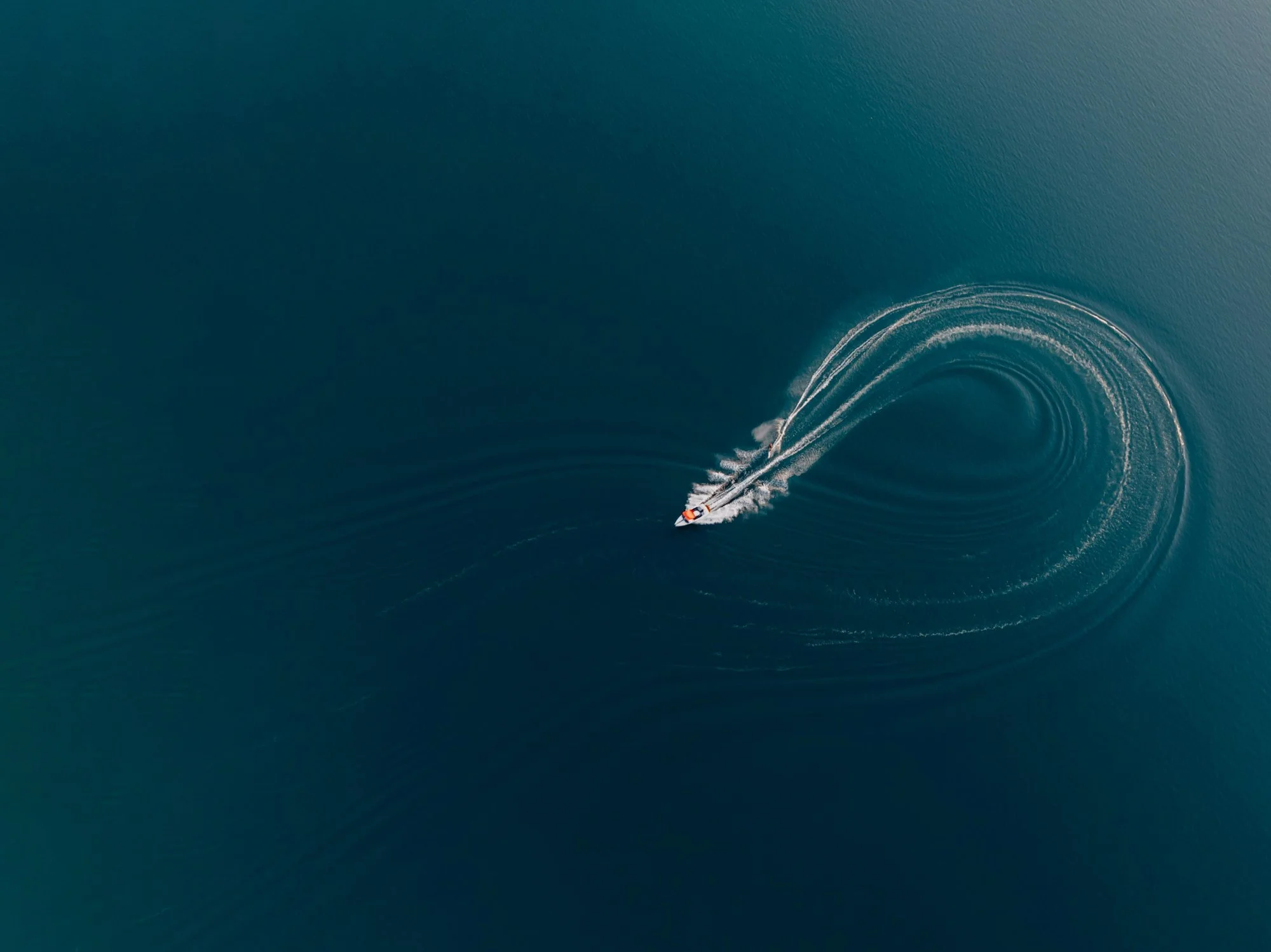 A boat speeding across the water, creating a large wake behind it, in an open body of water under a clear sky.