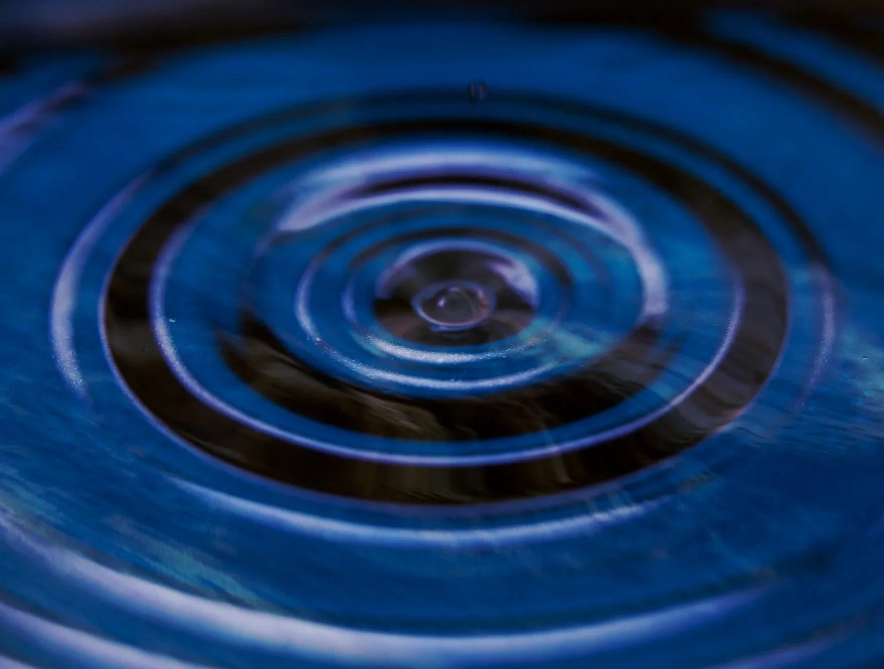 Close-up of a circular ripple pattern in dark blue water focused at the center with concentric ripples expanding outward.