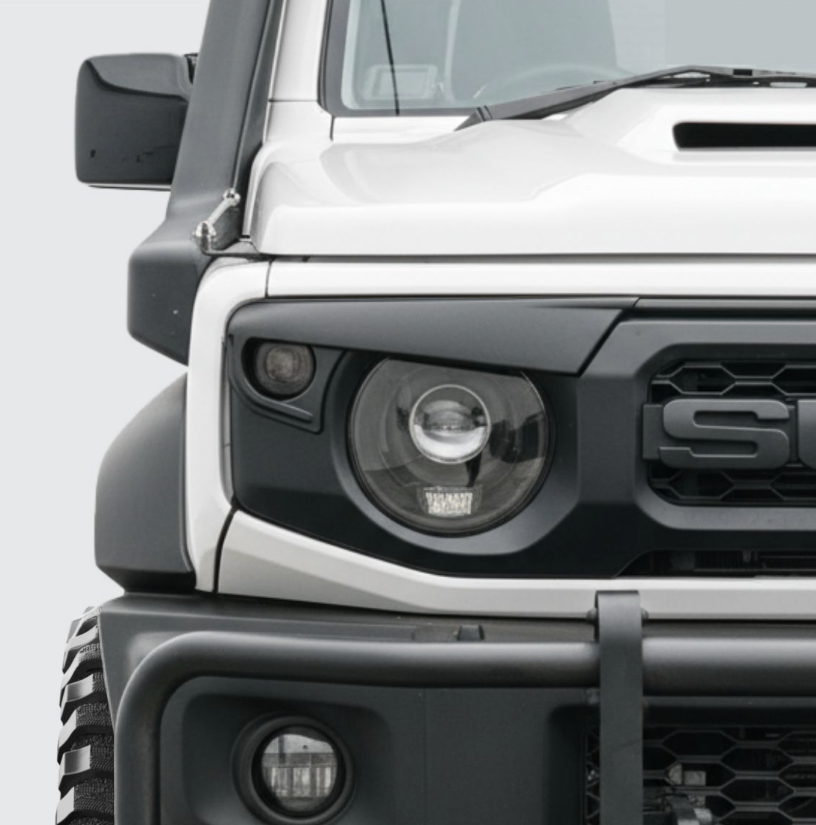 Close-up of the front portion of a white and black off-road vehicle, showing the headlight, grille, and a side mirror.