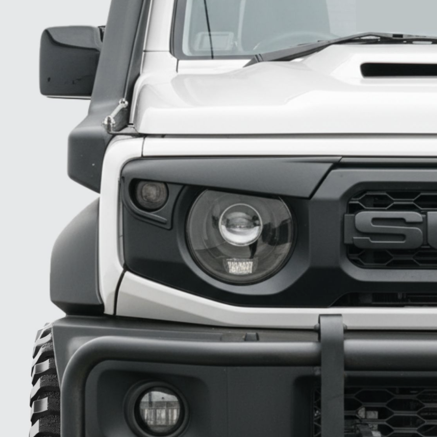 Close-up of the front of a white off-road SUV, showing the headlight, grille, and black bumper with a hook.