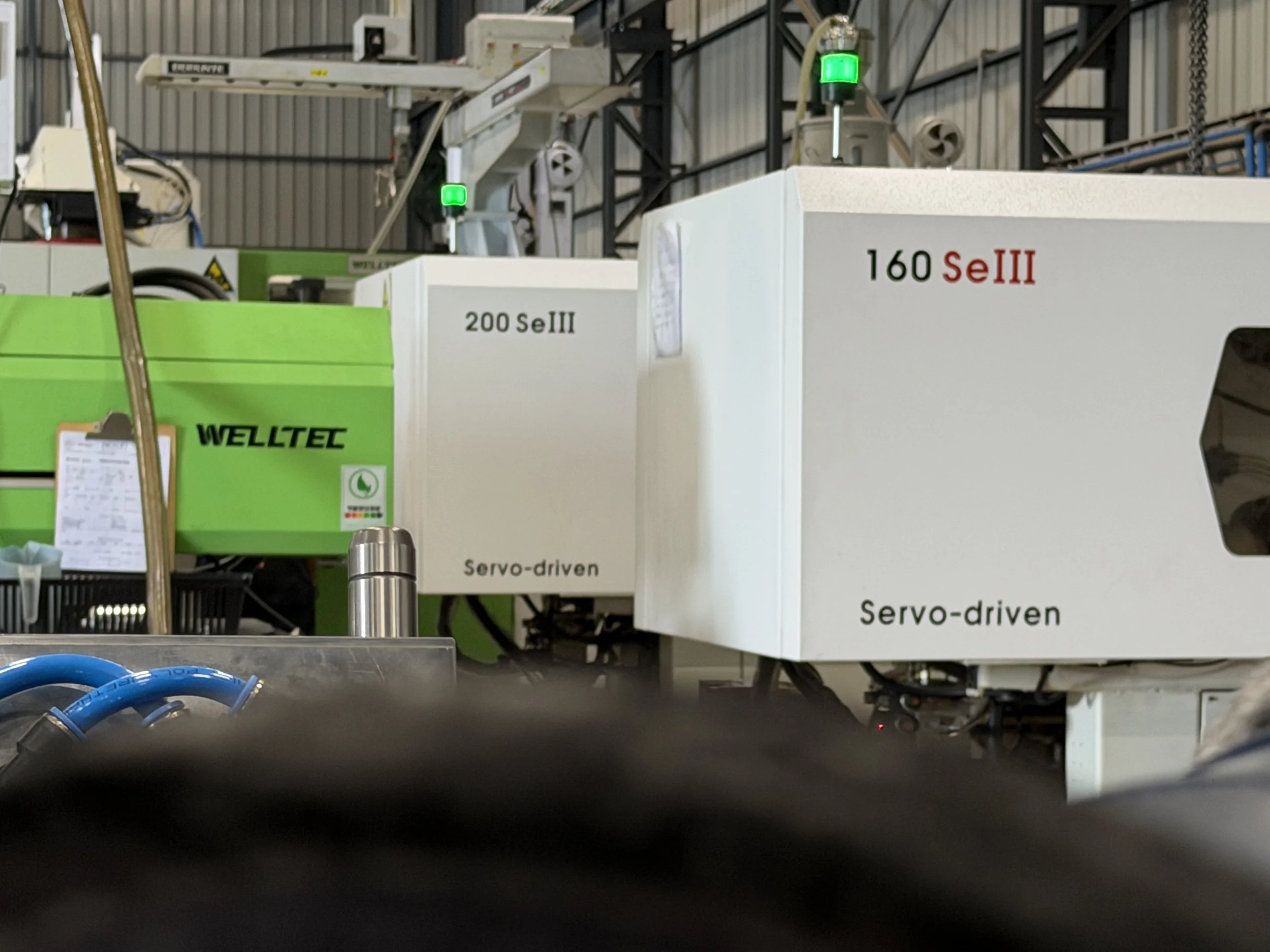Industrial robotic machines with labels '200 SeIII' and '160 SeIII', located inside a warehouse or factory, with various control panels and green indicator lights.