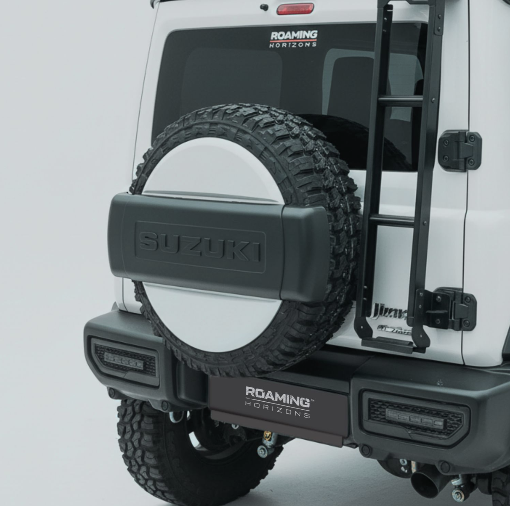 Close-up of the rear of a white Jeep vehicle featuring a mounted spare tire, a ladder, and a 'Roaming Horizons' logo on the back window and bumper.