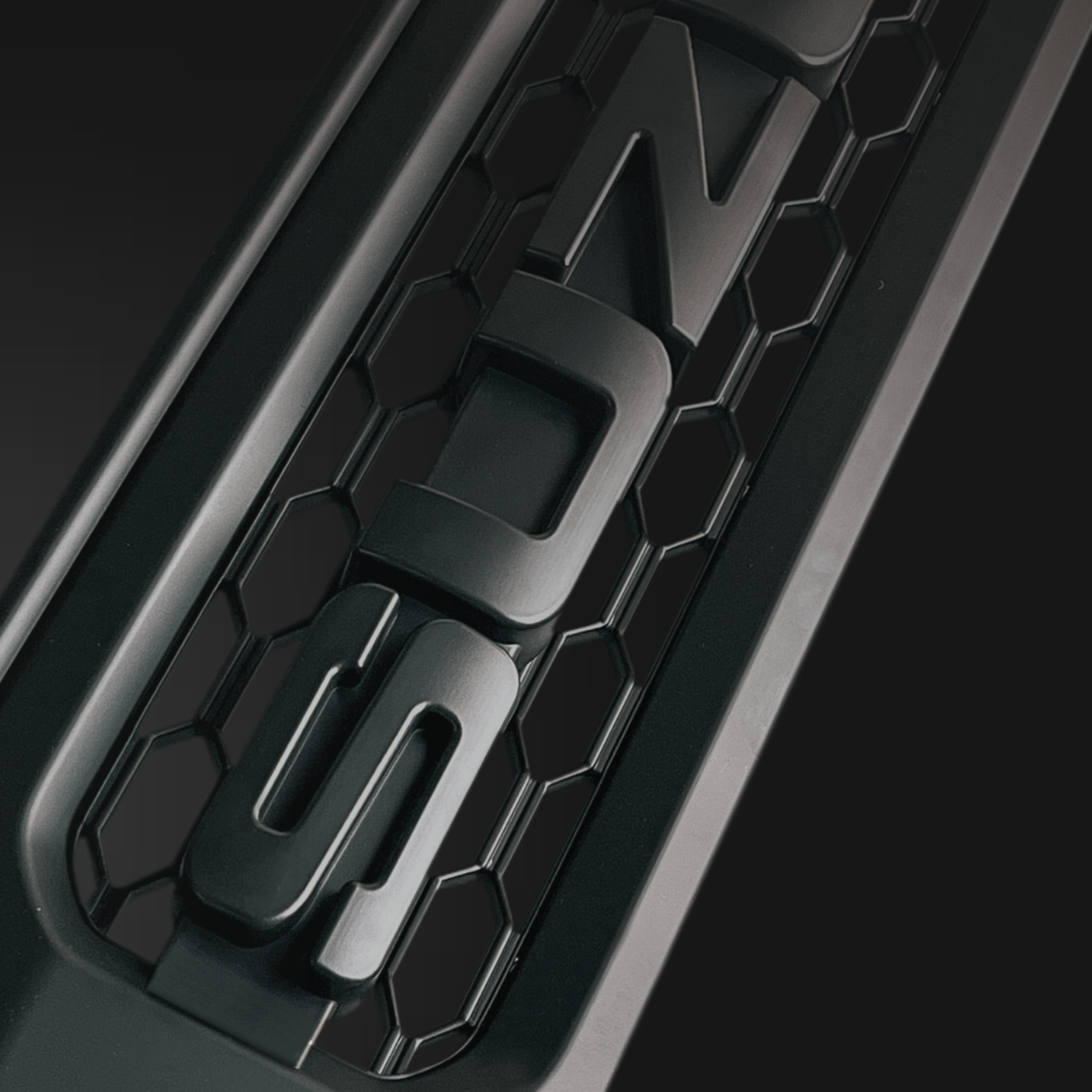 Close-up of a black vehicle grille with a hexagonal pattern and a logo in the center.