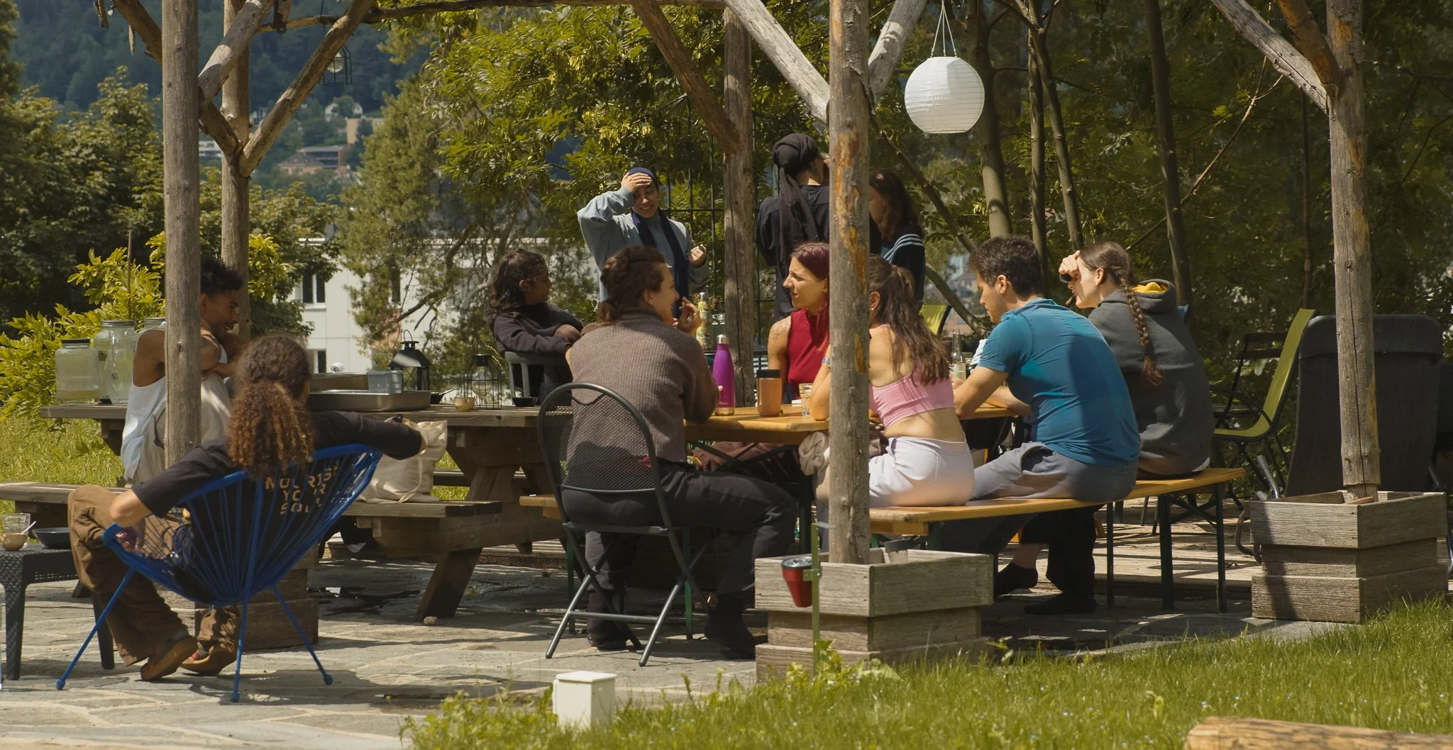 Groupe de personnes assises autour d'une table en plein air, discutant et profitant d'une journée ensoleillée dans un espace naturel.