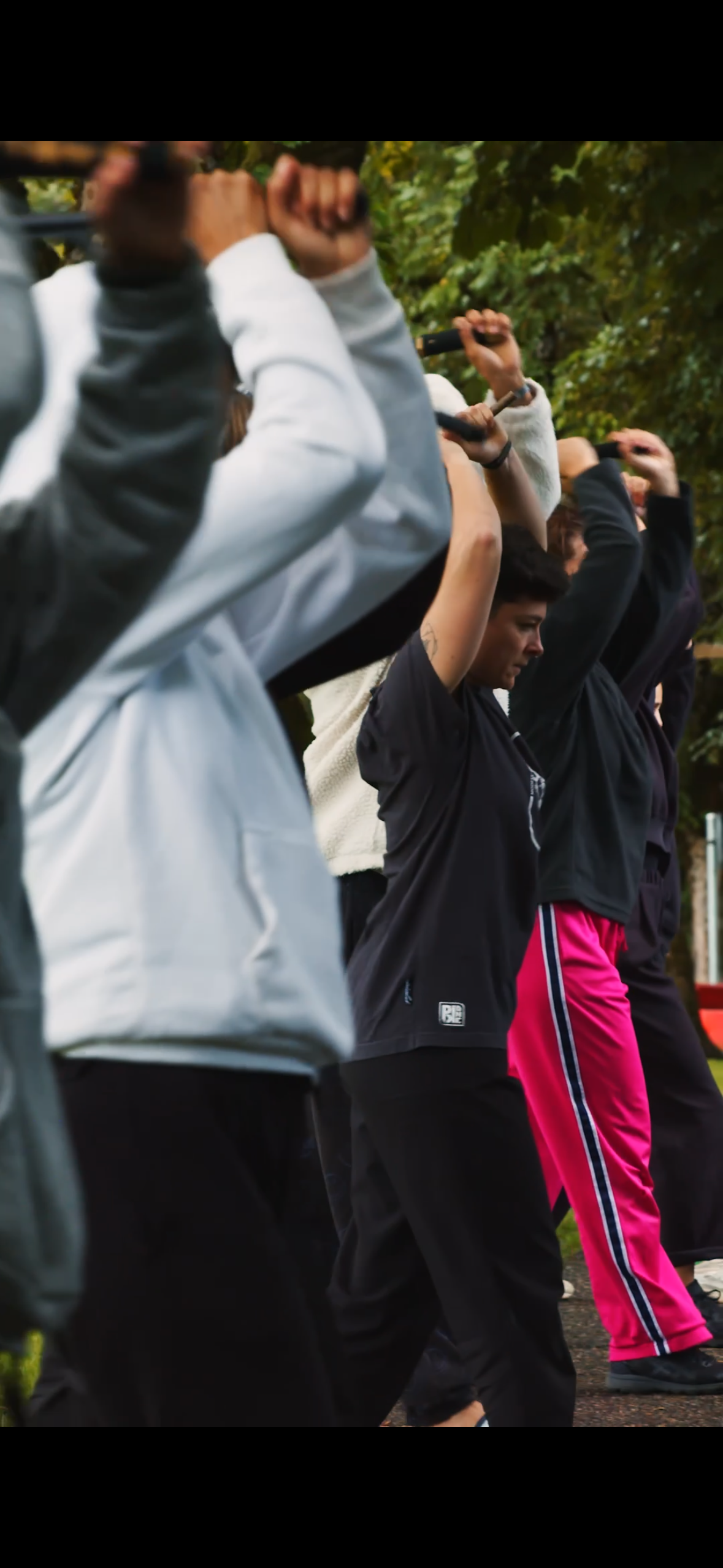 Groupe de personnes en tenue de sport effectuant une séance d'étirement ou d'exercice en extérieur, entre des arbres.
