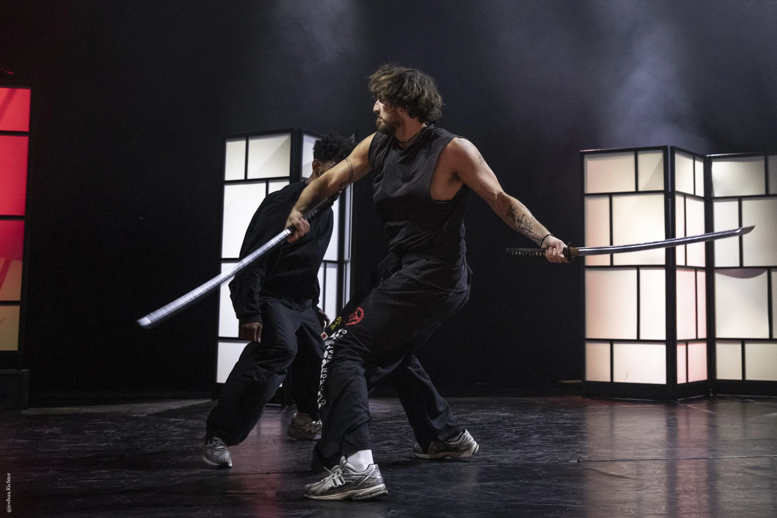 Deux hommes pratiquent des arts martiaux avec des épées dans une salle sombre avec des panneaux lumineux