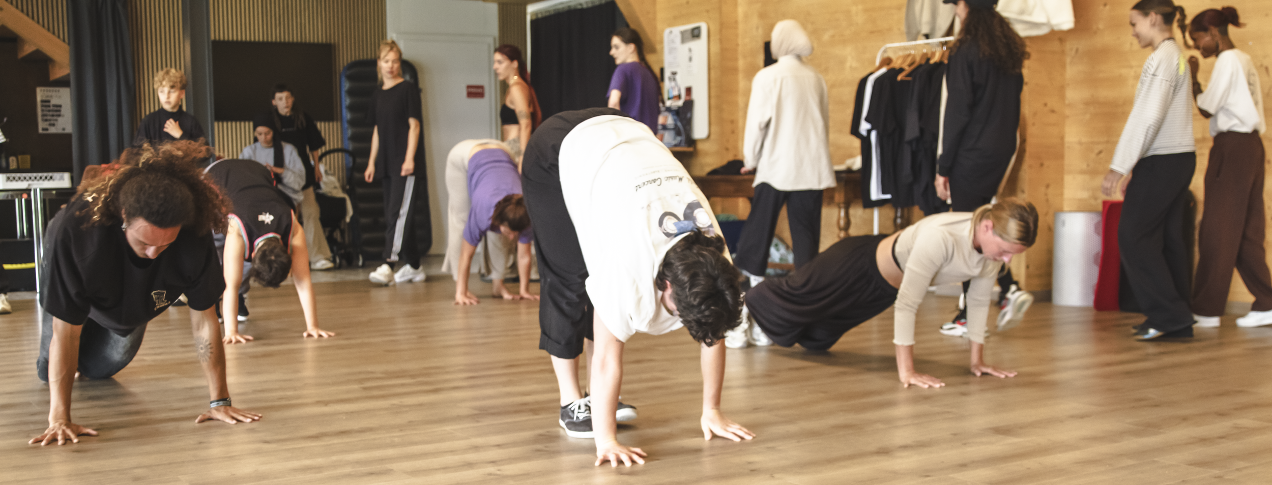Groupe de personnes participant à un cours de danse ou de fitness dans un studio, effectuant des exercices au sol, avec des vêtements décontractés et une ambiance dynamique.