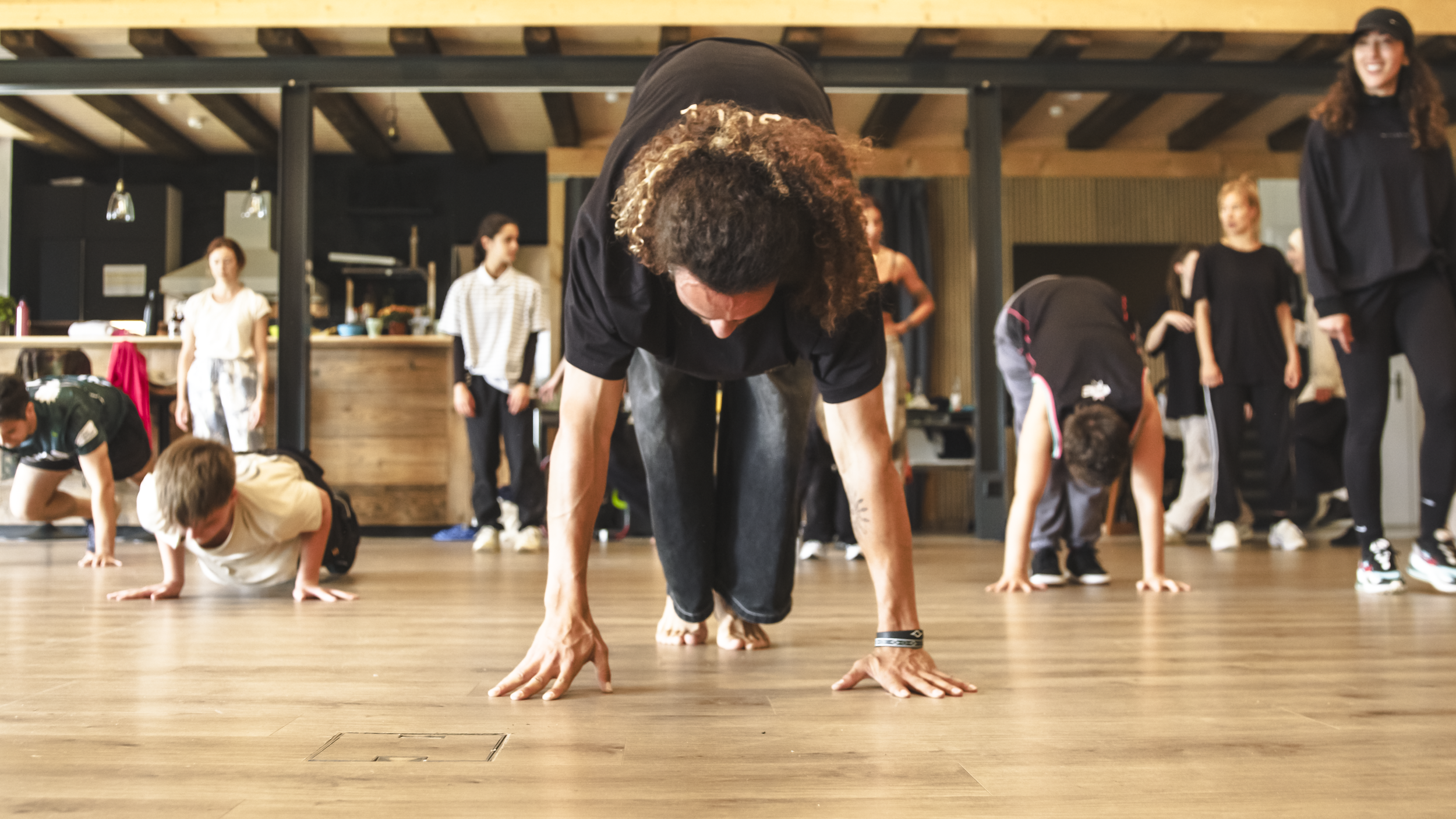 Groupe de personnes, y compris des enfants, participant à une séance d'entraînement ou de yoga dans une salle intérieure avec un sol en bois.