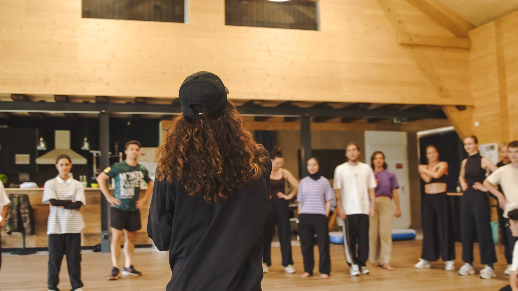 Groupe de personnes écoutant une femme avec un chapeau noir dans un espace intérieur en bois