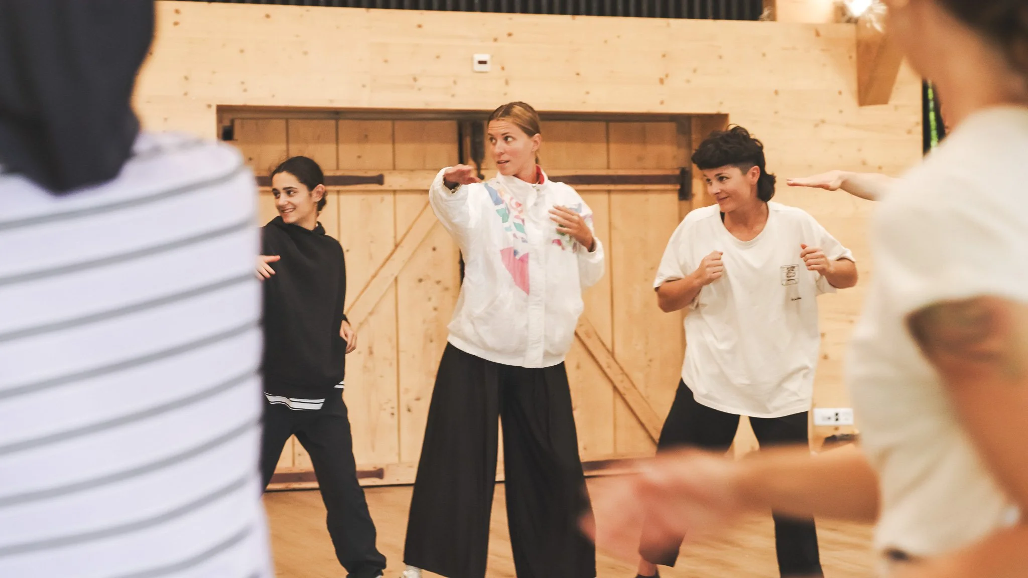 Un groupe de personnes participant à un cours de danse ou de fitness dans une salle avec murs en bois, avec un instructeur en blanc au centre.
