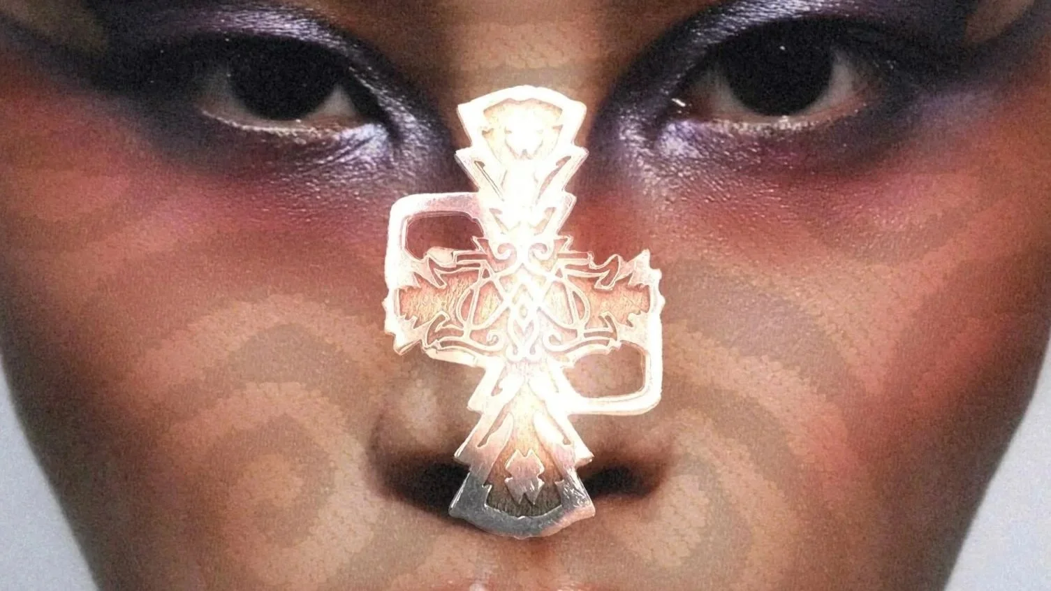Close-up d'un visage avec un tatouage ou une décoration en forme de croix stylisée en métal sur le nez.