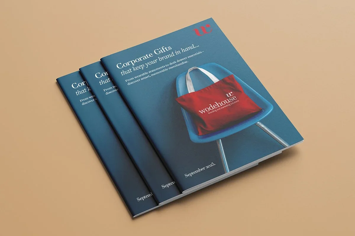Three corporate gift catalogs with a blue cover featuring a red tote bag on a blue chair, titled 'Corporate Gifts that keep your brand in hand...' on a beige background.