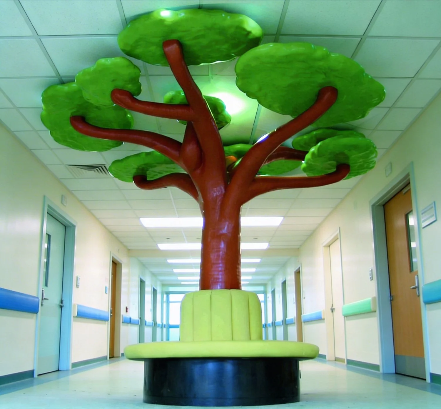 Colorful tree-shaped bench in hospital hallway with beige walls and multiple closed doors.