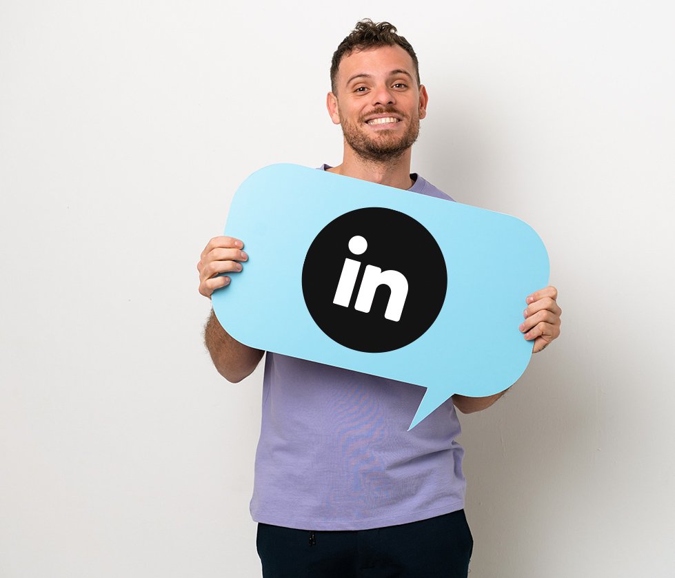 A smiling man holding a blue speech bubble sign with the LinkedIn logo on it.