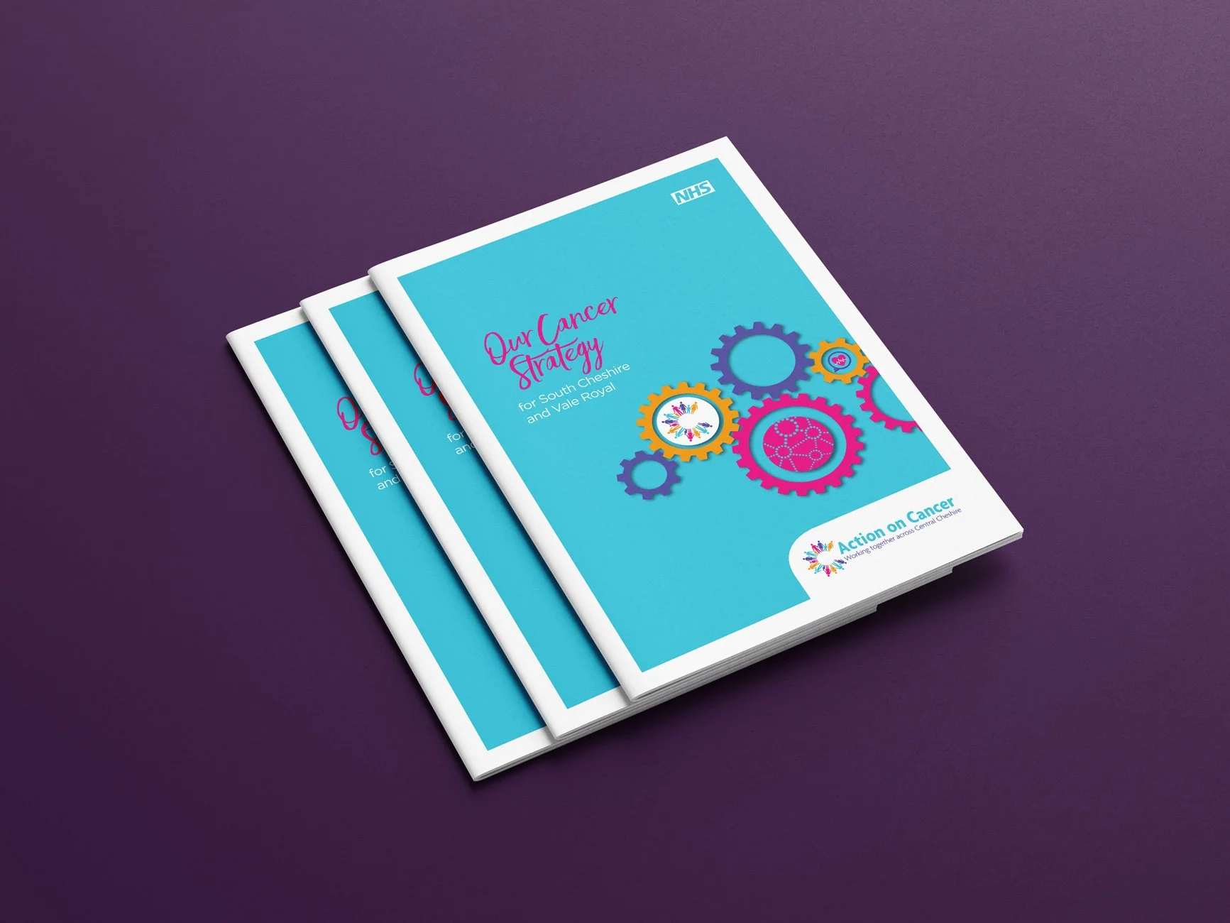 Three copies of a printed report titled "Our Cancer Strategy for South Cheshire and Vale Royal" with a blue cover, colorful gear illustrations, and the Action on Cancer logo, lying on a purple surface.
