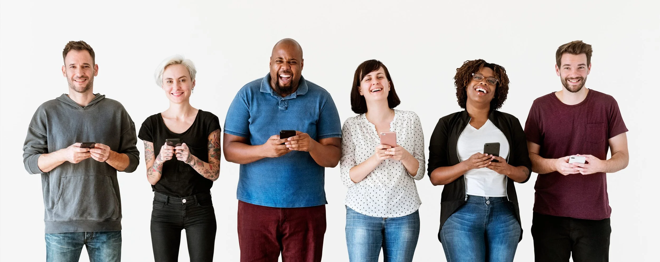 Six diverse people standing in a row, smiling, and looking at their smartphones in front of a plain white background.