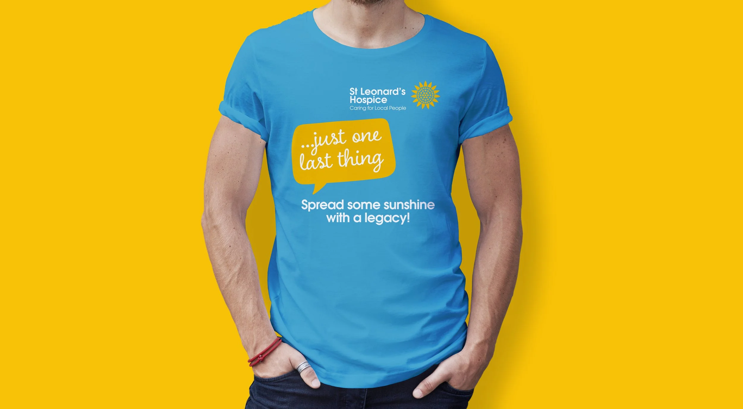 Blue T-shirt with yellow and white printed text and logo, worn by a person with arms in pockets, yellow background, promoting St Leonard's Hospice, with phrases 'just one last thing' and 'Spread some sunshine with a legacy!'