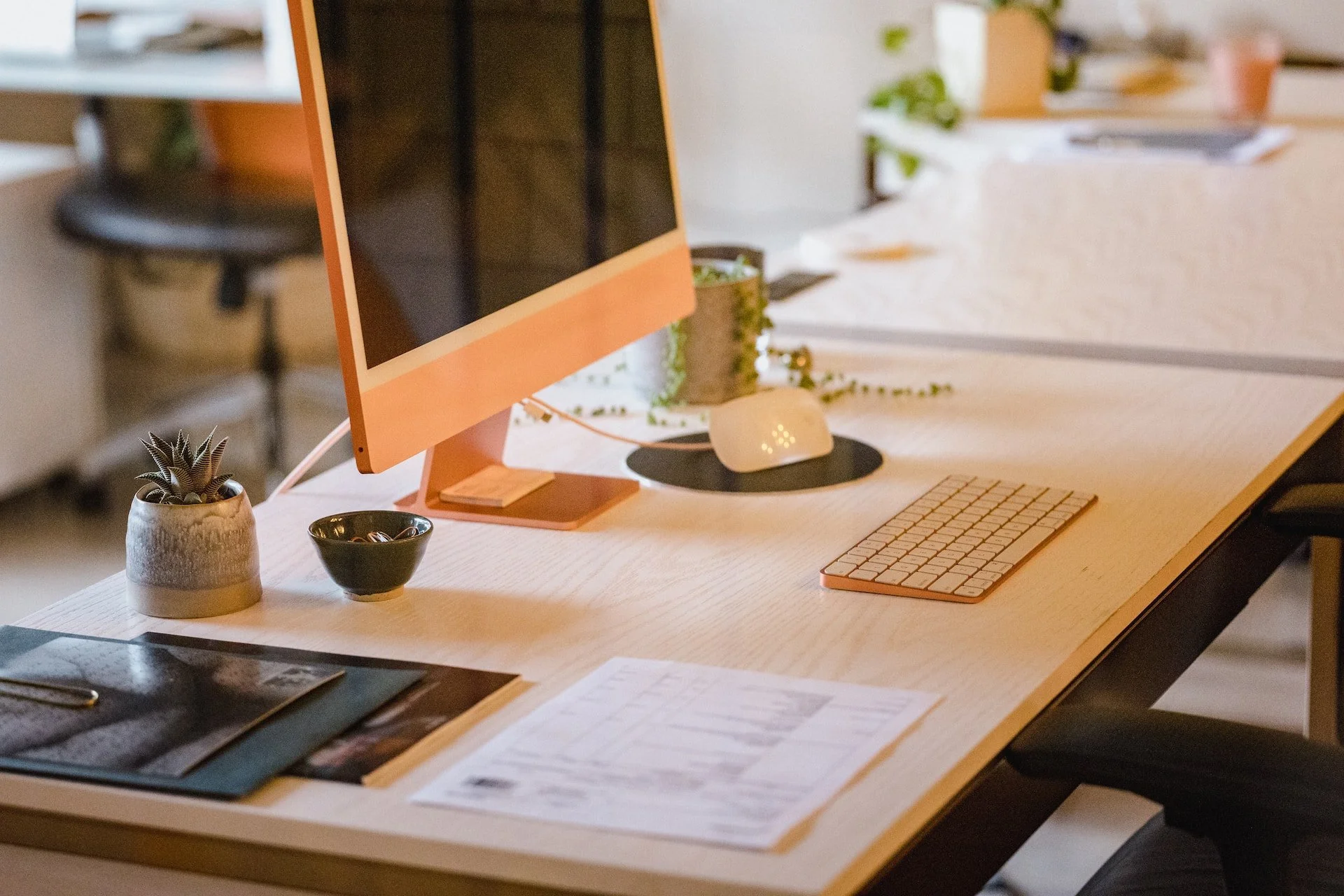 A modern workspace with a computer, keyboard, mouse, potted plant, documents, and office supplies on a wooden desk.