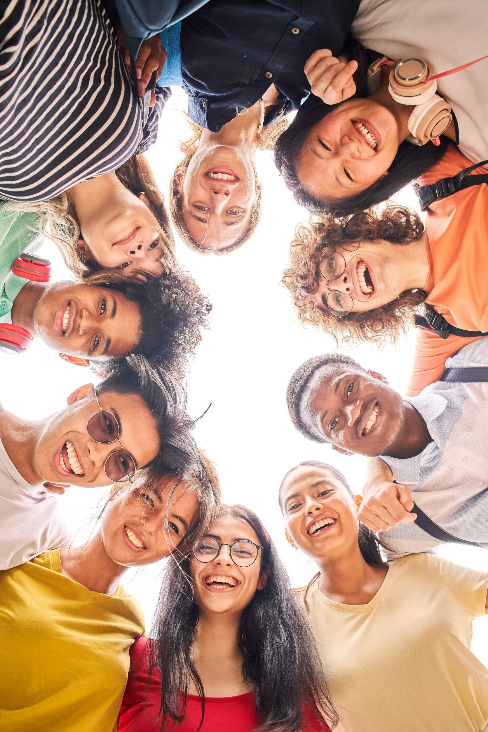 Group of diverse young adults smiling and looking down into the camera as they stand in a circle.