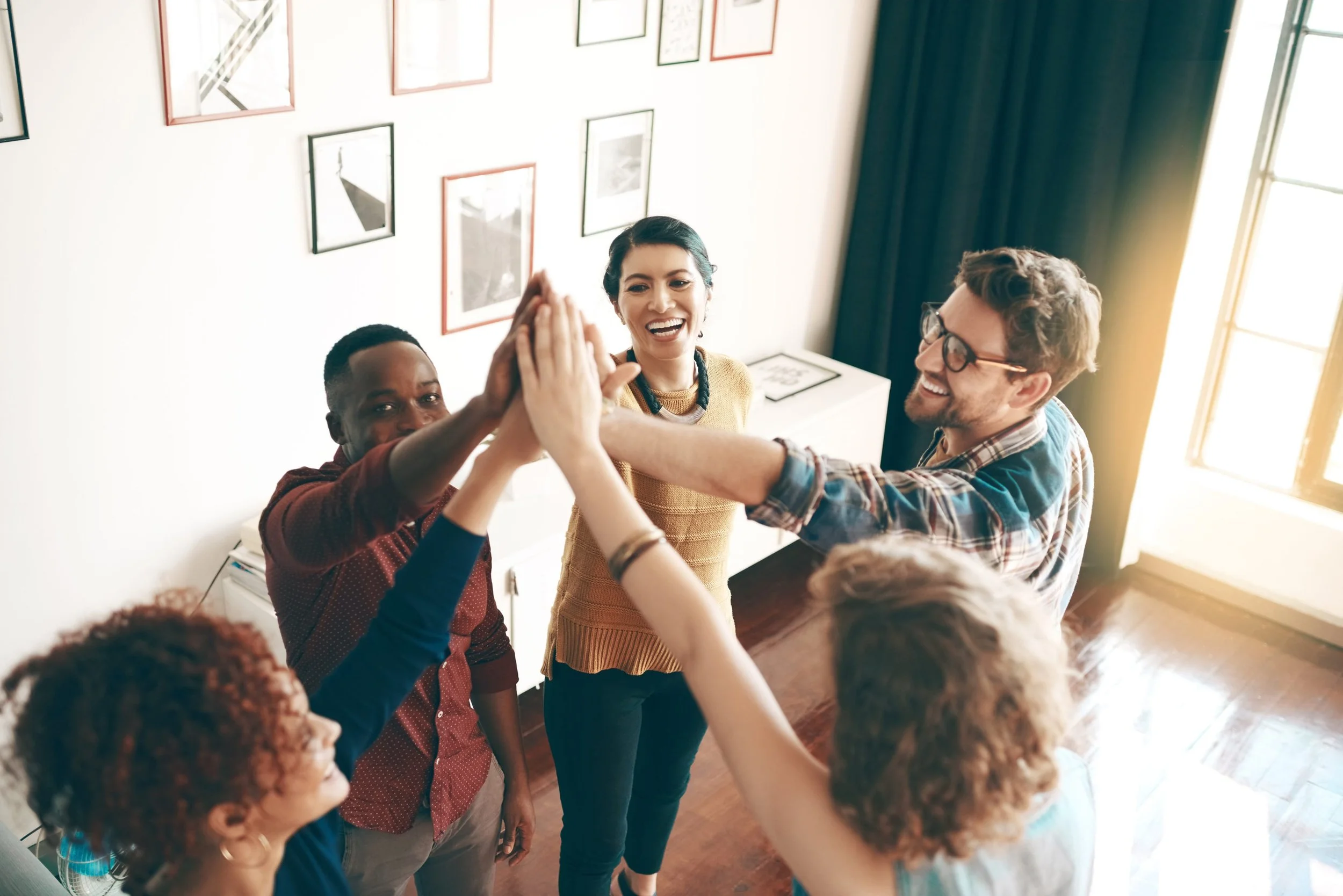 A group of diverse people giving high-fives indoors, smiling and celebrating.