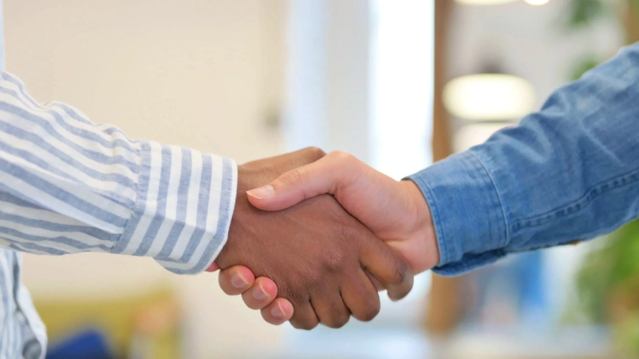 Two people shaking hands, one wearing a striped shirt and the other a blue denim shirt.