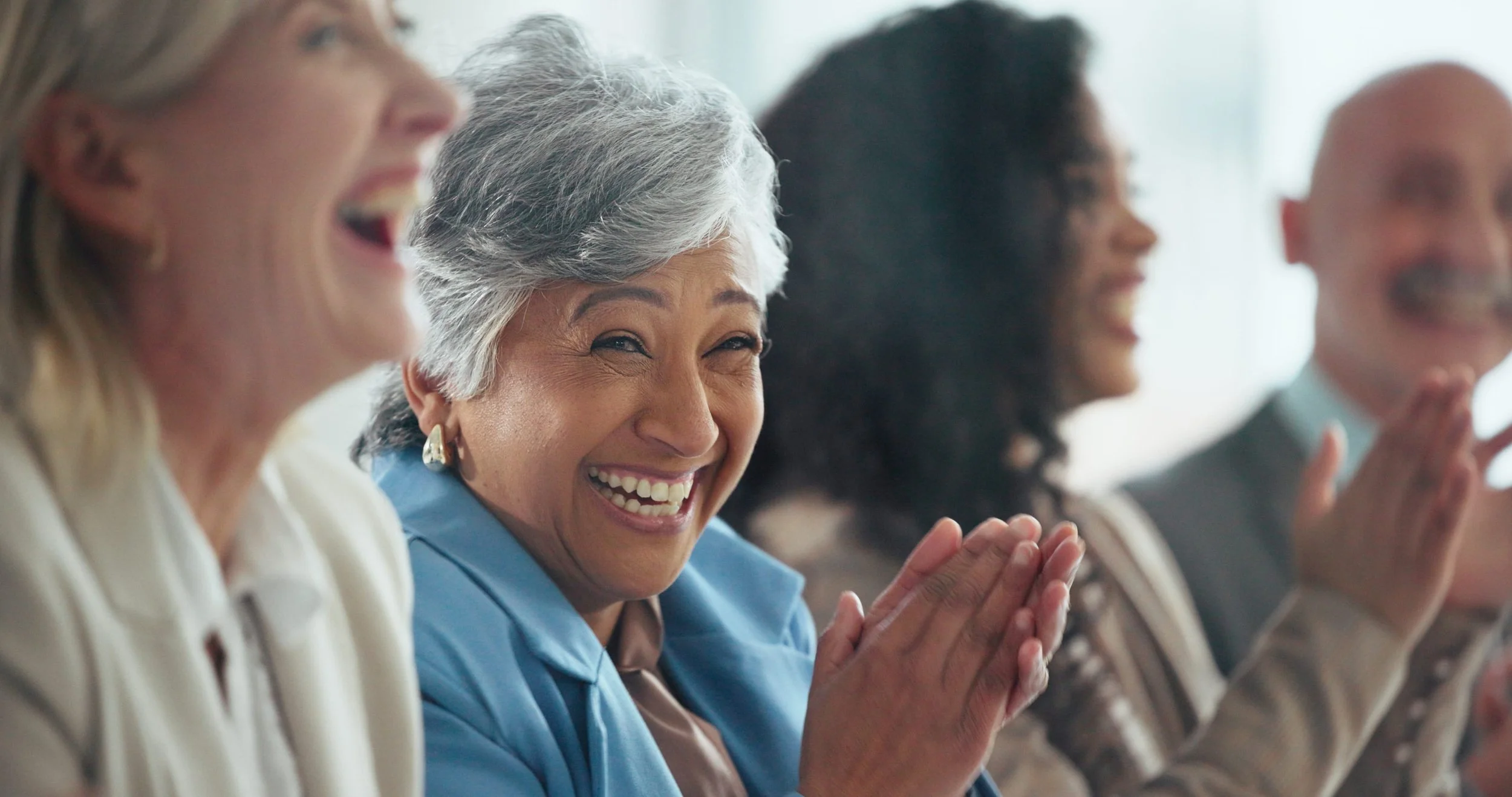 Four diverse women sitting together, smiling and clapping during a conference or gathering.