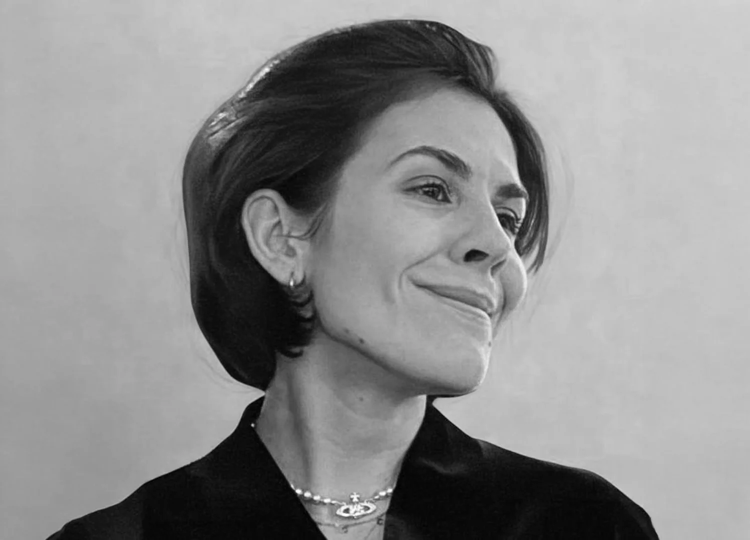 A black and white portrait of a smiling woman with short, styled hair, wearing earrings, a pearl necklace, and a dark top.
