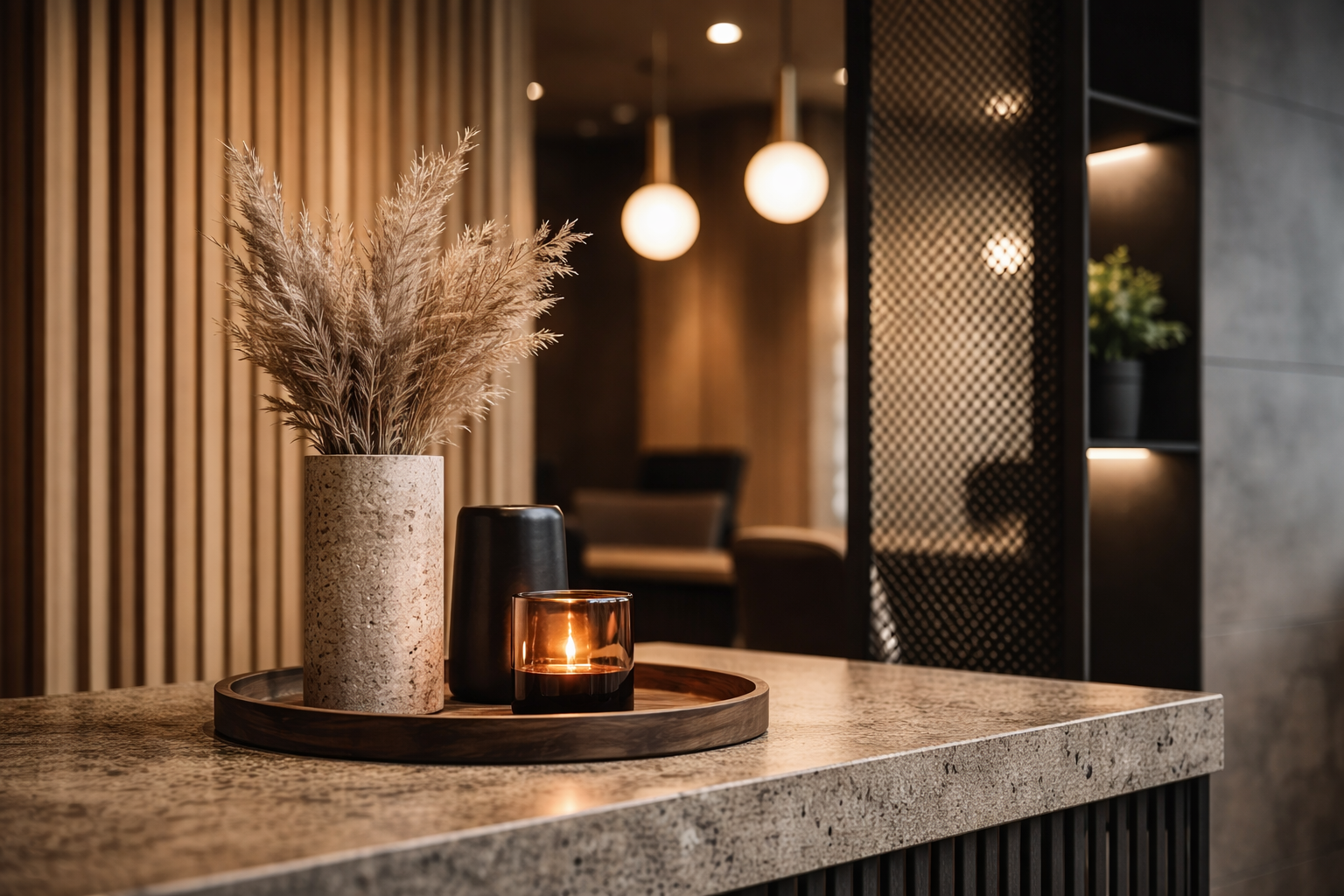 Modern interior with a speckled stone countertop, a tray holding a tall floral arrangement, a candle, and vases, in a warmly lit space.