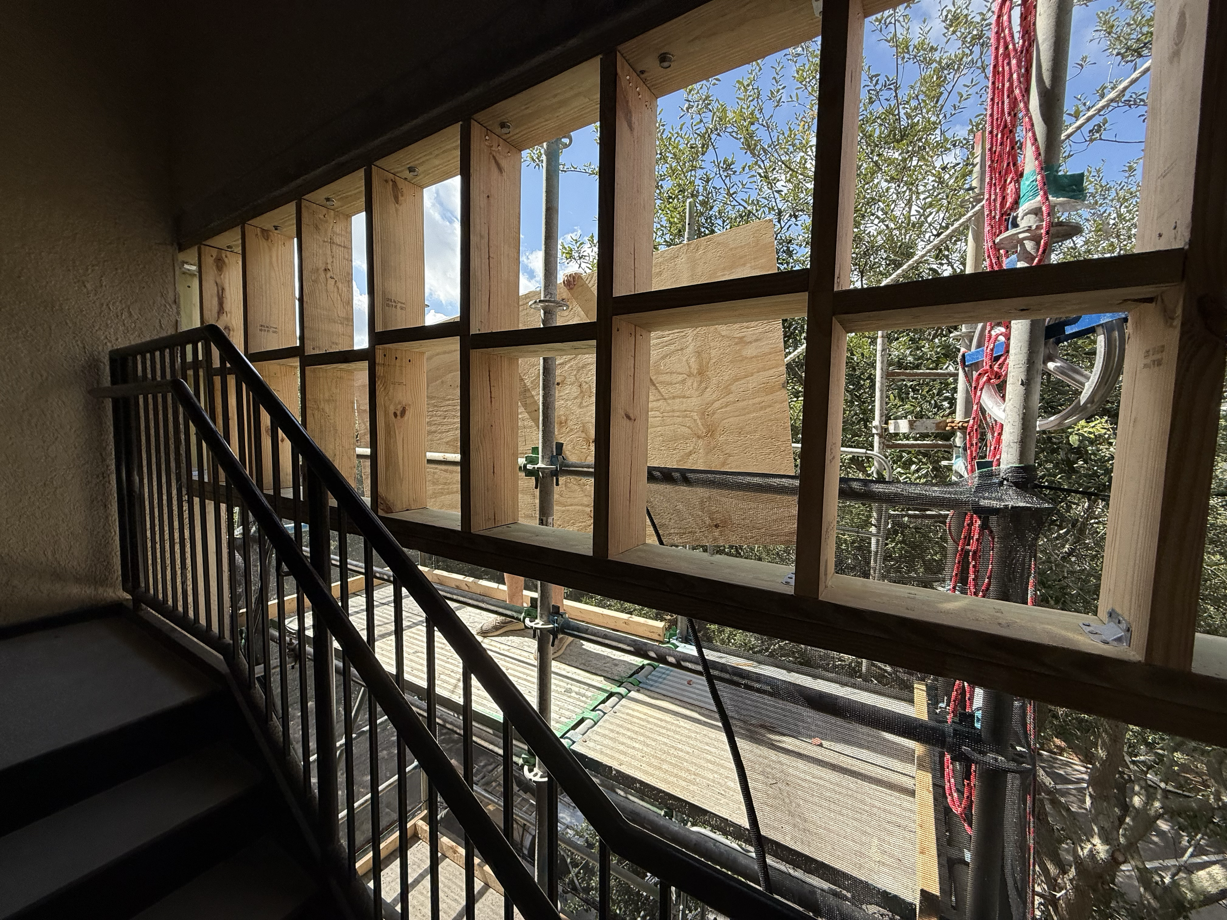 Building under construction showing wooden framing and scaffolding outside window.