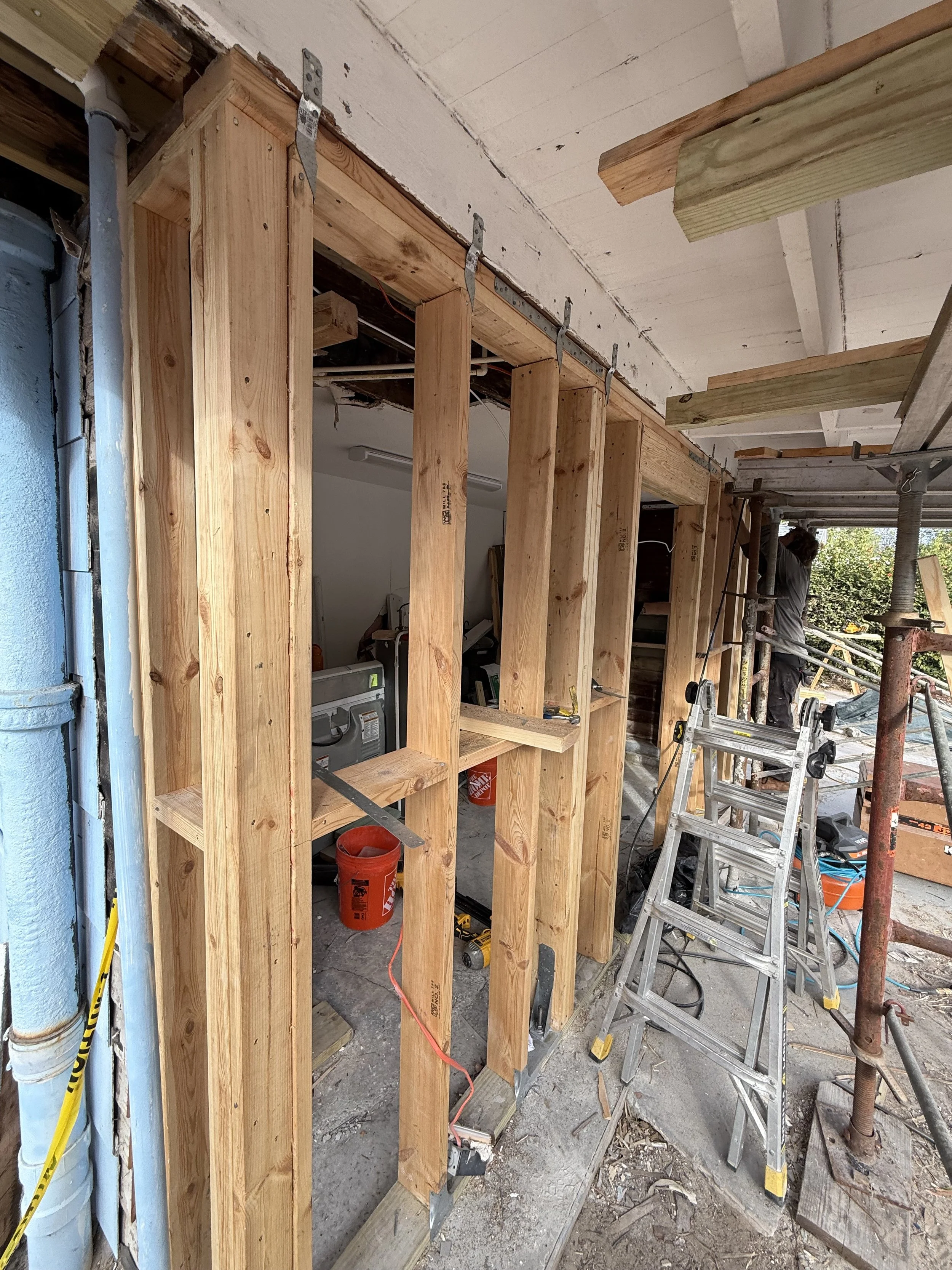 Wood framing for a wall under construction, with scaffolding and tools around, inside a building.