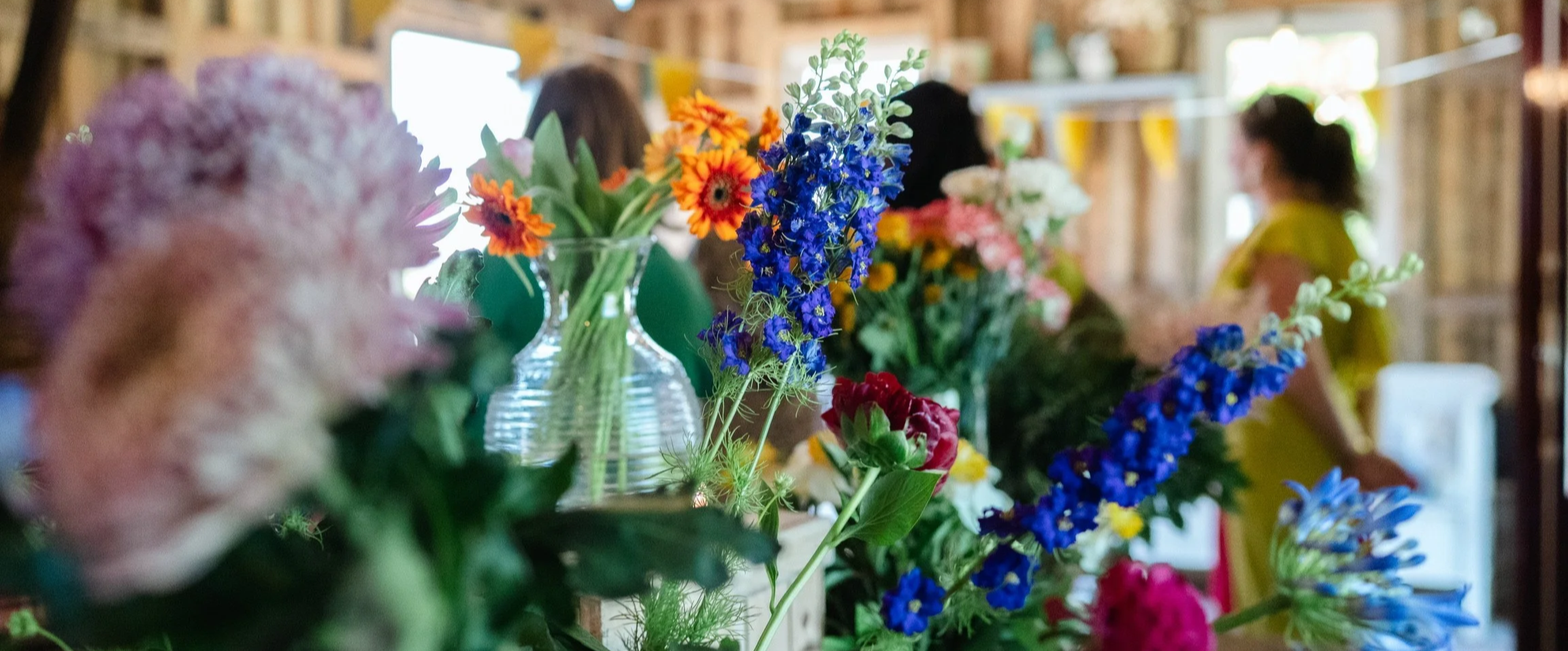 Vases filled with colorful flowers, with blurred people in the background at an indoor event.