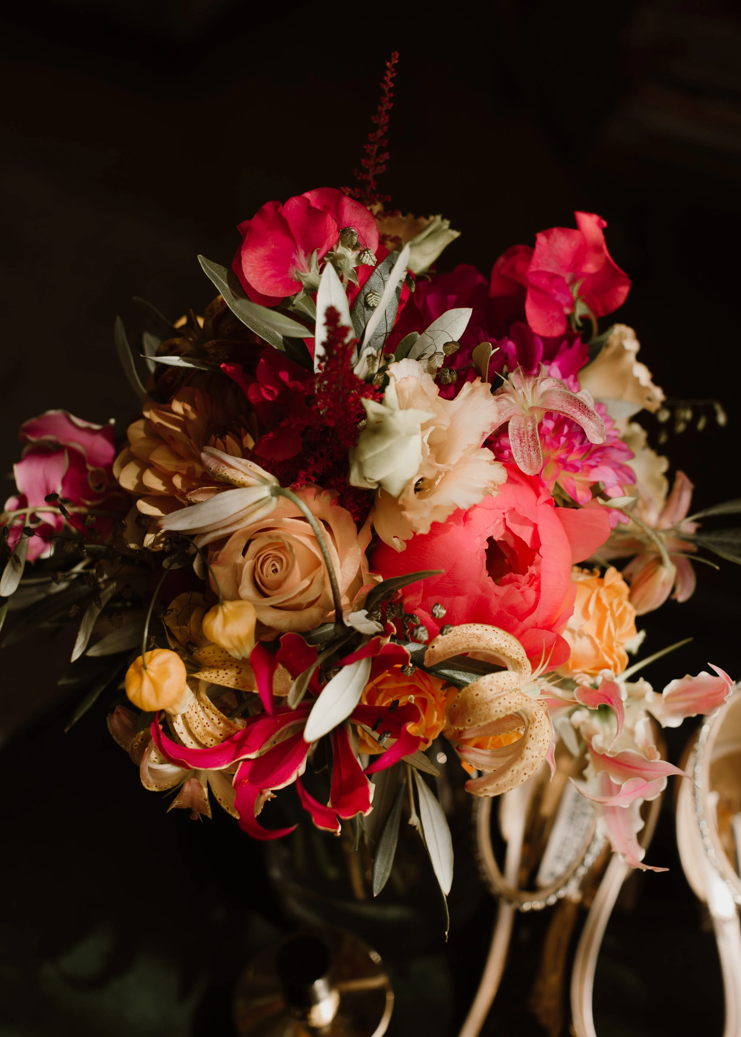 A colorful bouquet of various flowers including roses, lilies, and other blossoms, set against a dark background.