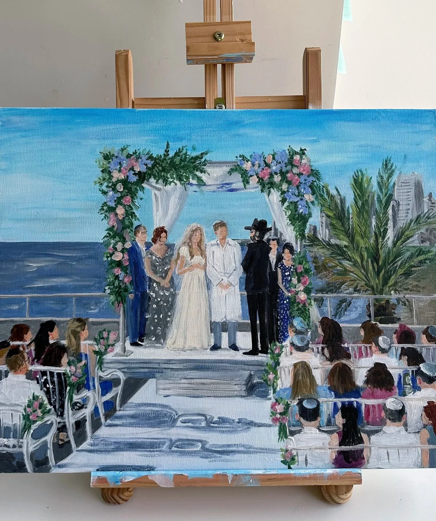Painting of a wedding ceremony on a boat deck with the ocean in the background, decorated with flowers and white drapes, with guests seated and the couple standing under an arch.