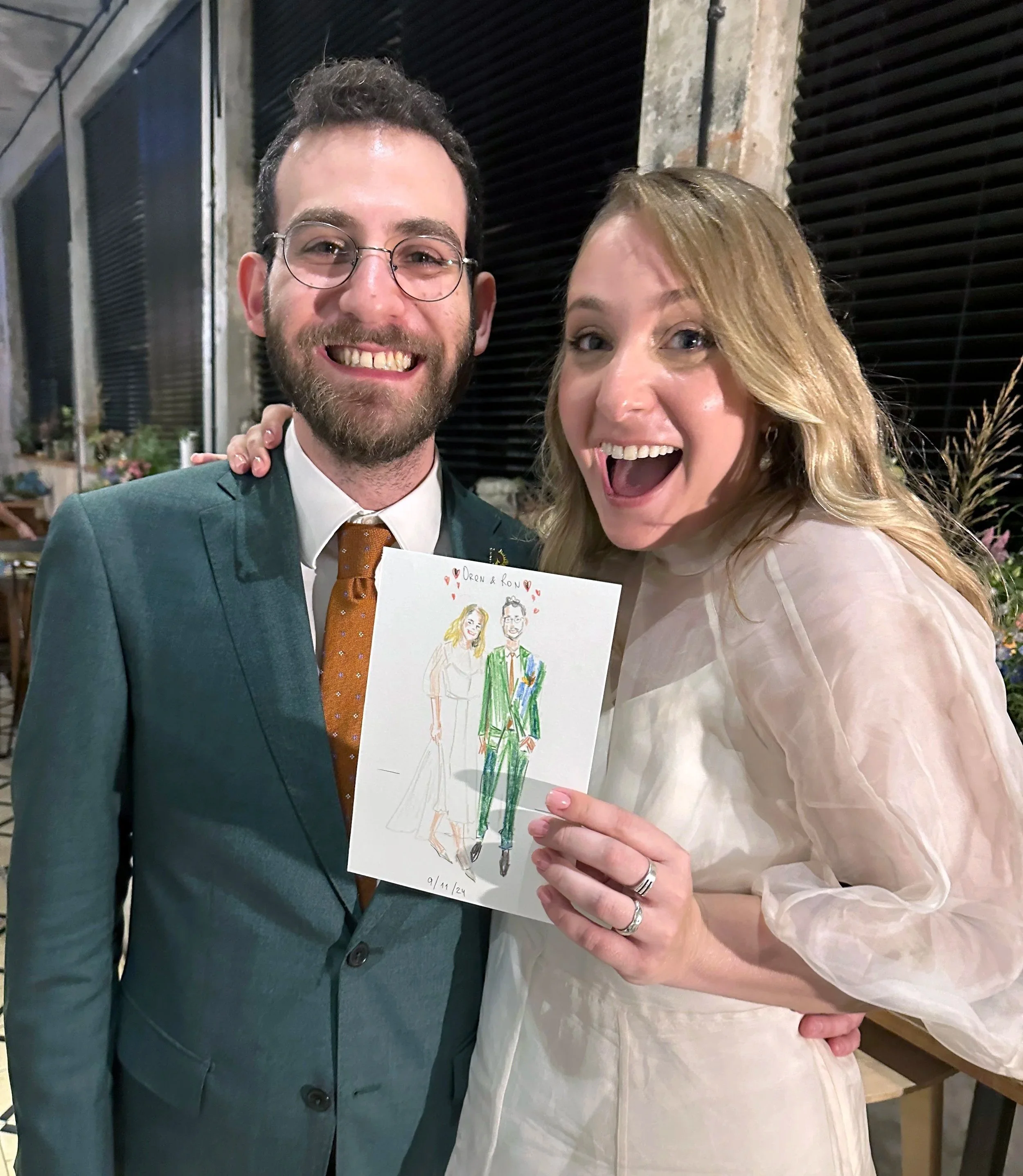 A smiling couple holding a wedding drawing at a celebration.