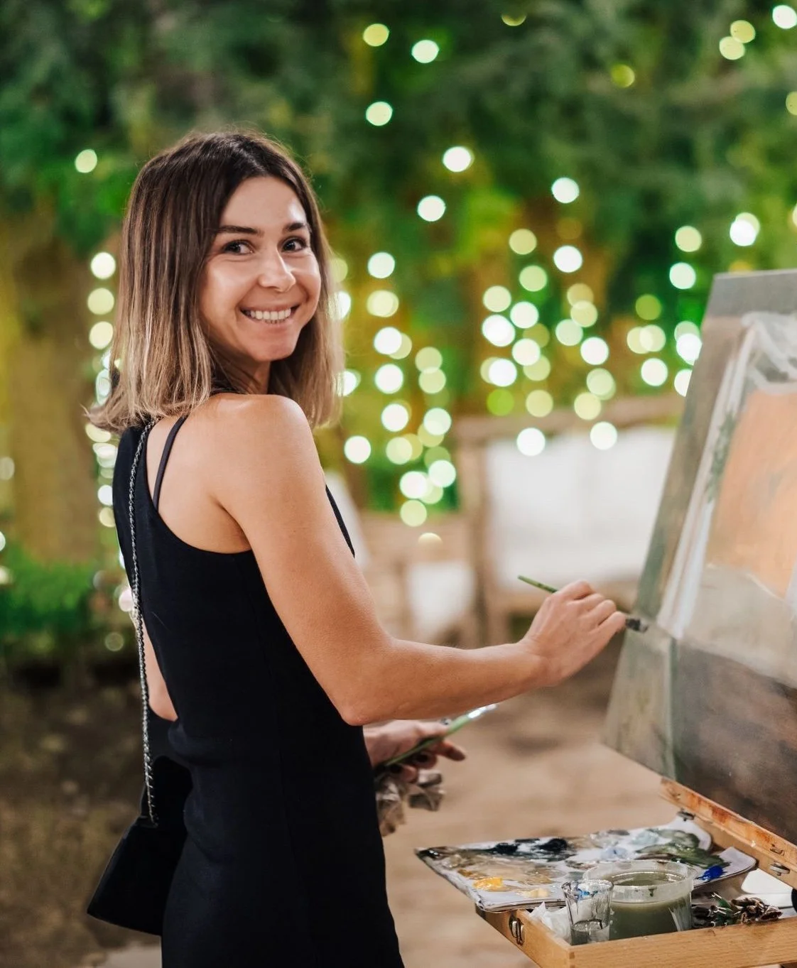A live event artist smiling and painting outdoors at the wedding venue, surrounded by celebration lights.