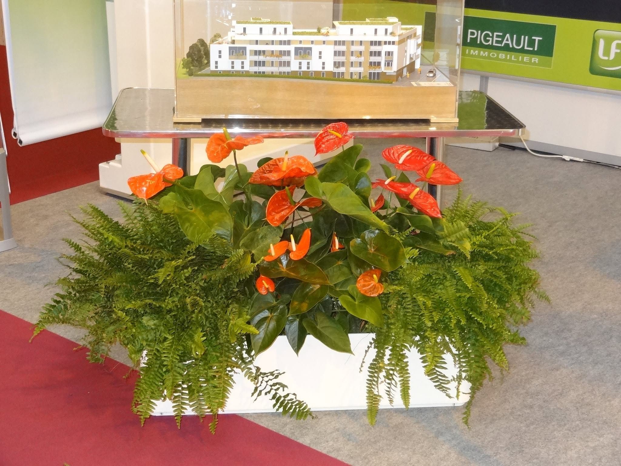 Modèle réduit d'un bâtiment résidentiel blanc avec plusieurs étages, visible derrière une vitre, entouré de plantes vertes dans un display.