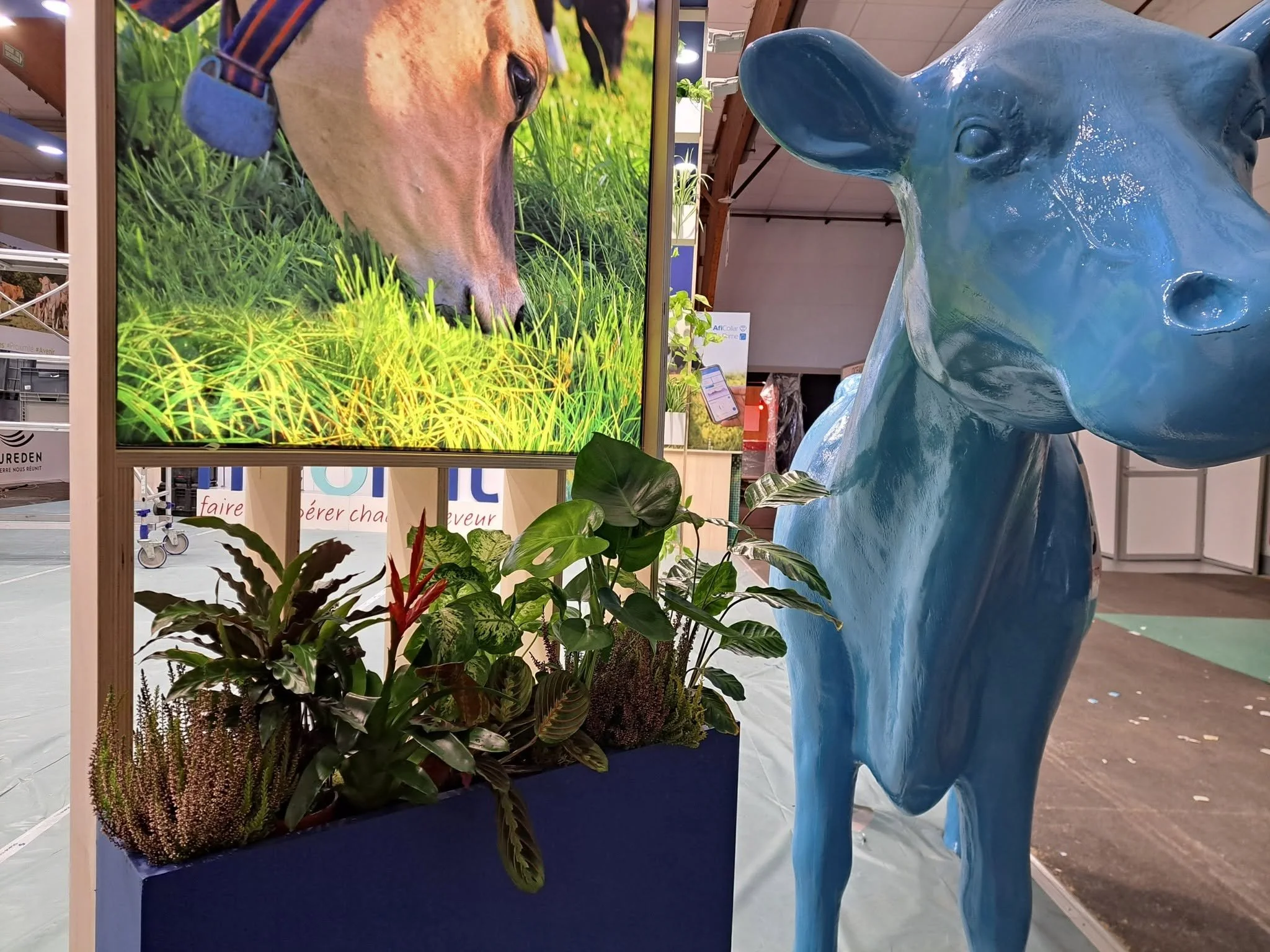 Un panneau avec une image d'un chien mangeant de l'herbe, entouré de plusieurs plantes vertes, avec une sculpture bleue d'un animal à côté.