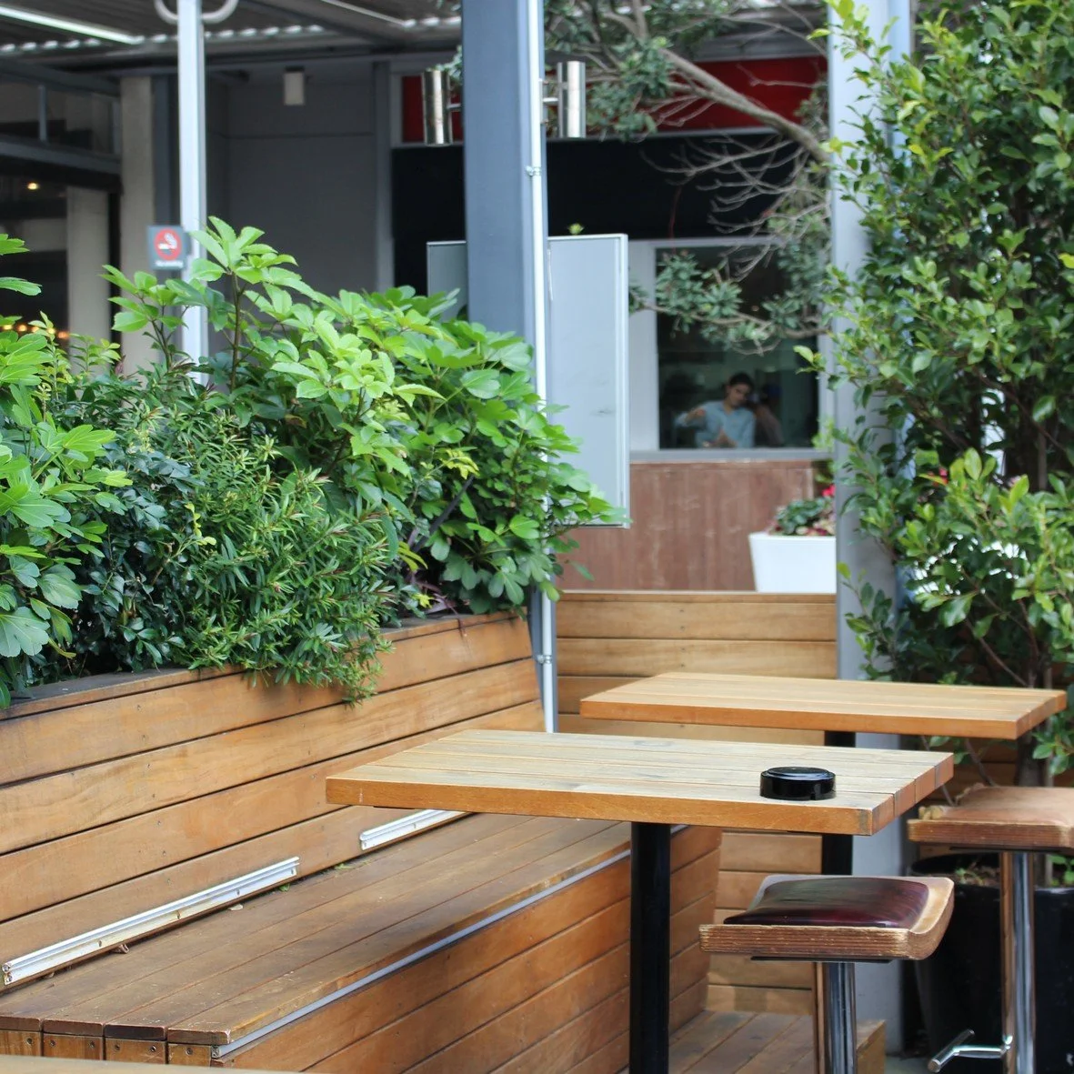 Terrasse extérieure avec tables en bois, banc intégré, et plantes vertes