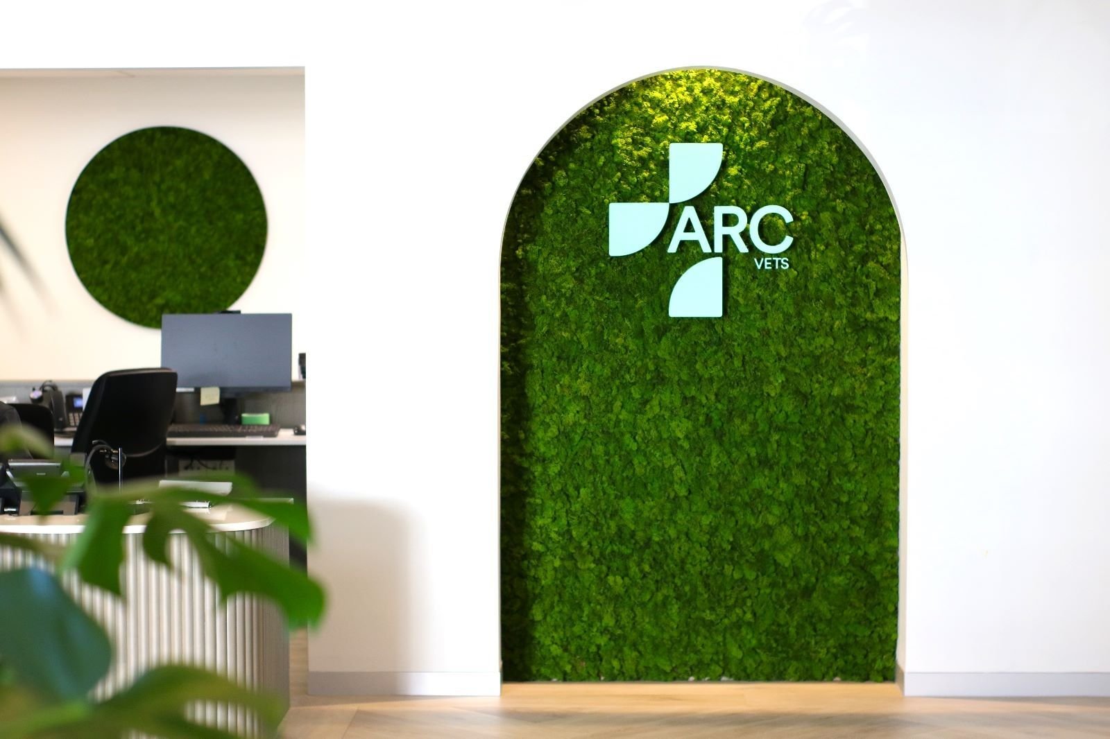 Mur végétal avec le logo 'ARC VETS' encadré d'un arc, dans un bureau moderne.