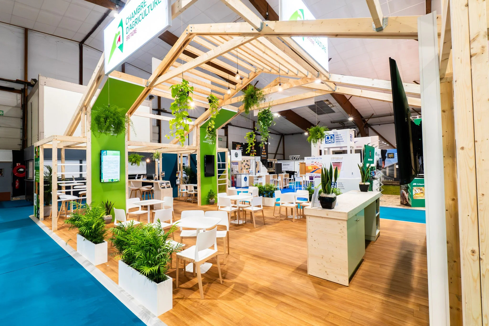 Stand d'agriculture avec des plantes suspendues et des assises blanches, décor en bois clair, panneaux d'information, dans un grand hall d'exposition.