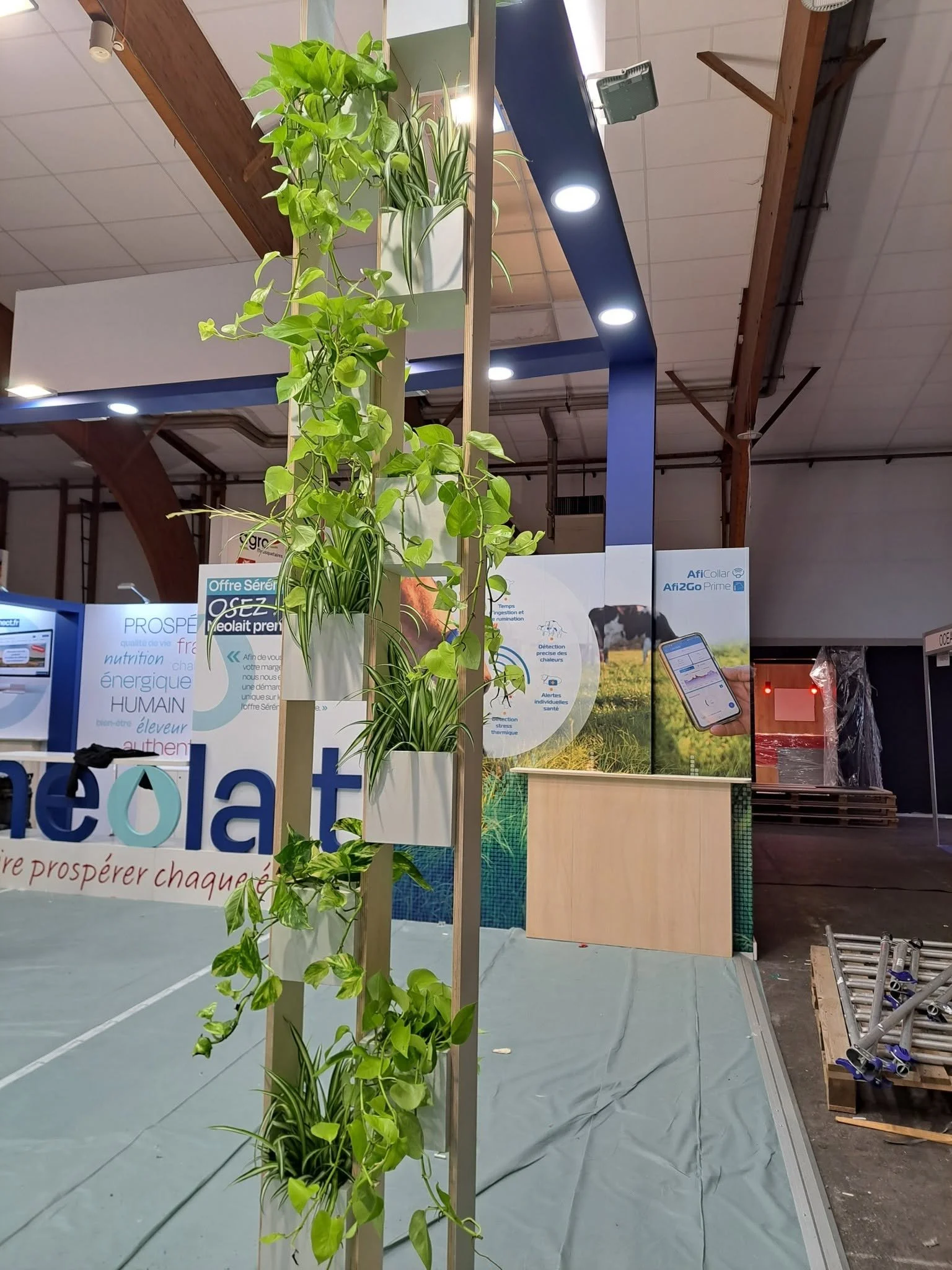 Plantes vertes suspendues à une structure dans un espace intérieur avec des panneaux d'affichage et des équipements lumineux