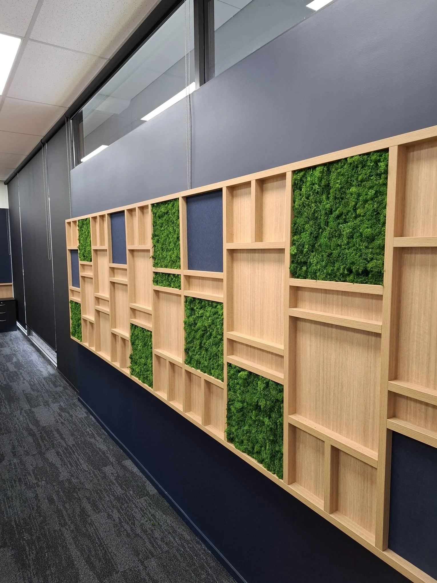 Panneau en bois avec des sections remplies de mousse végétale verte, fixé contre un mur dans un bureau.